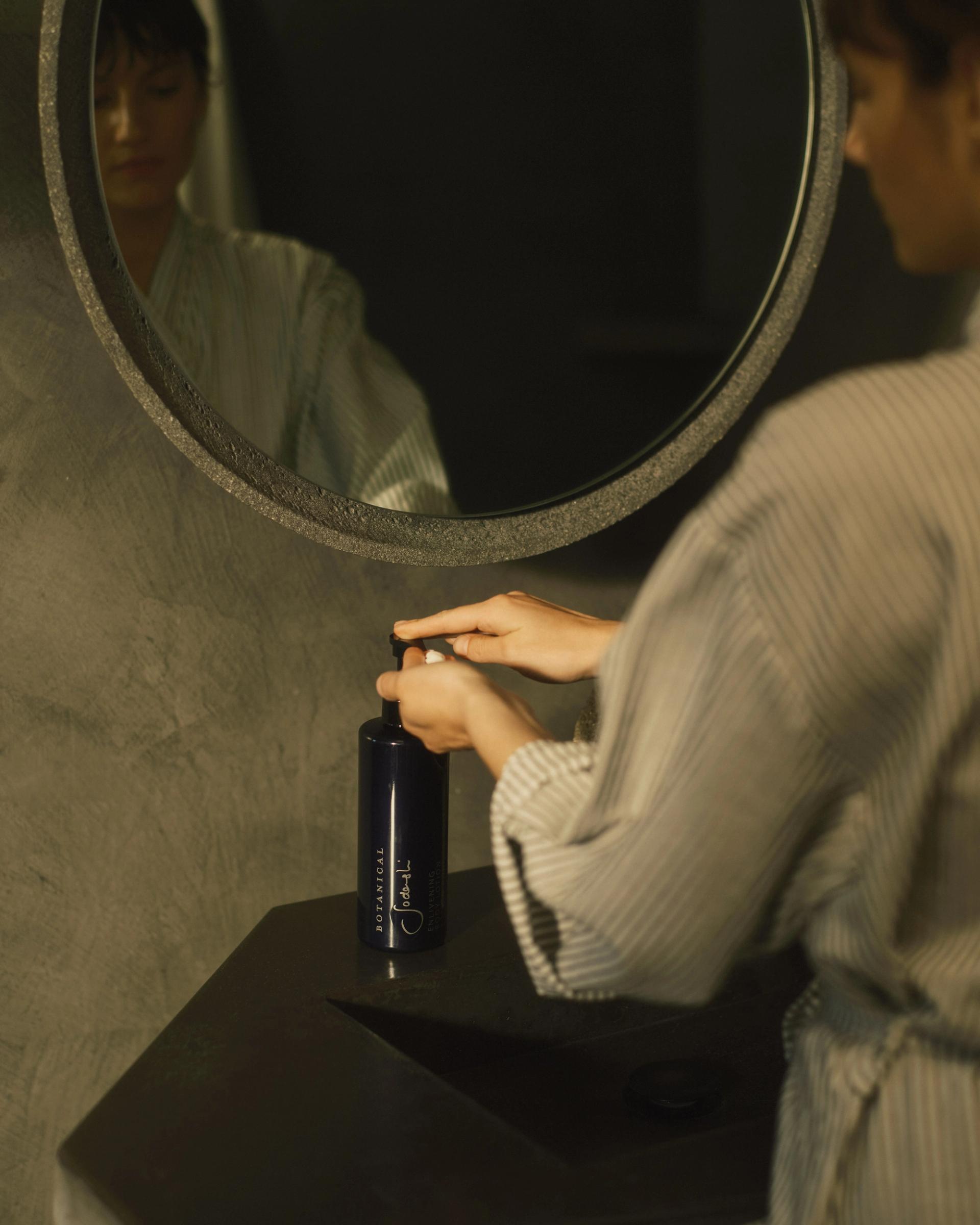 Woman in robe using Sodashi Body Lotion dispenser on bathroom vanity