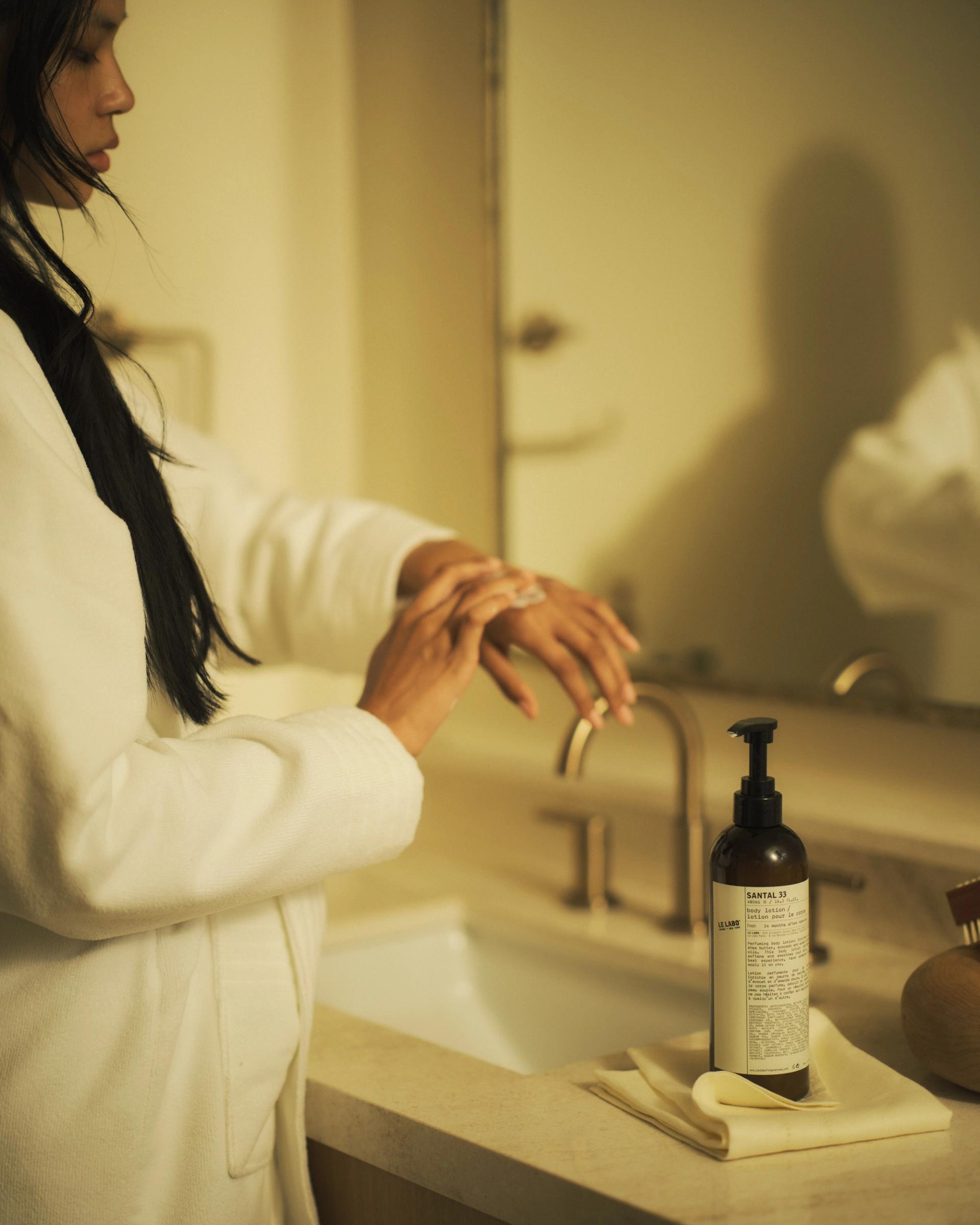 Woman in bathroom applying Le Labo Santal 33 Body Lotion on hands