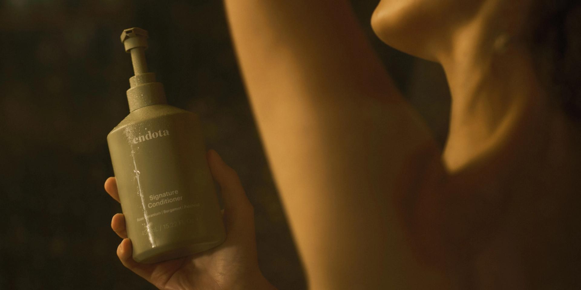 Girl in Shower holding a bottle of endota Signature Conditioner