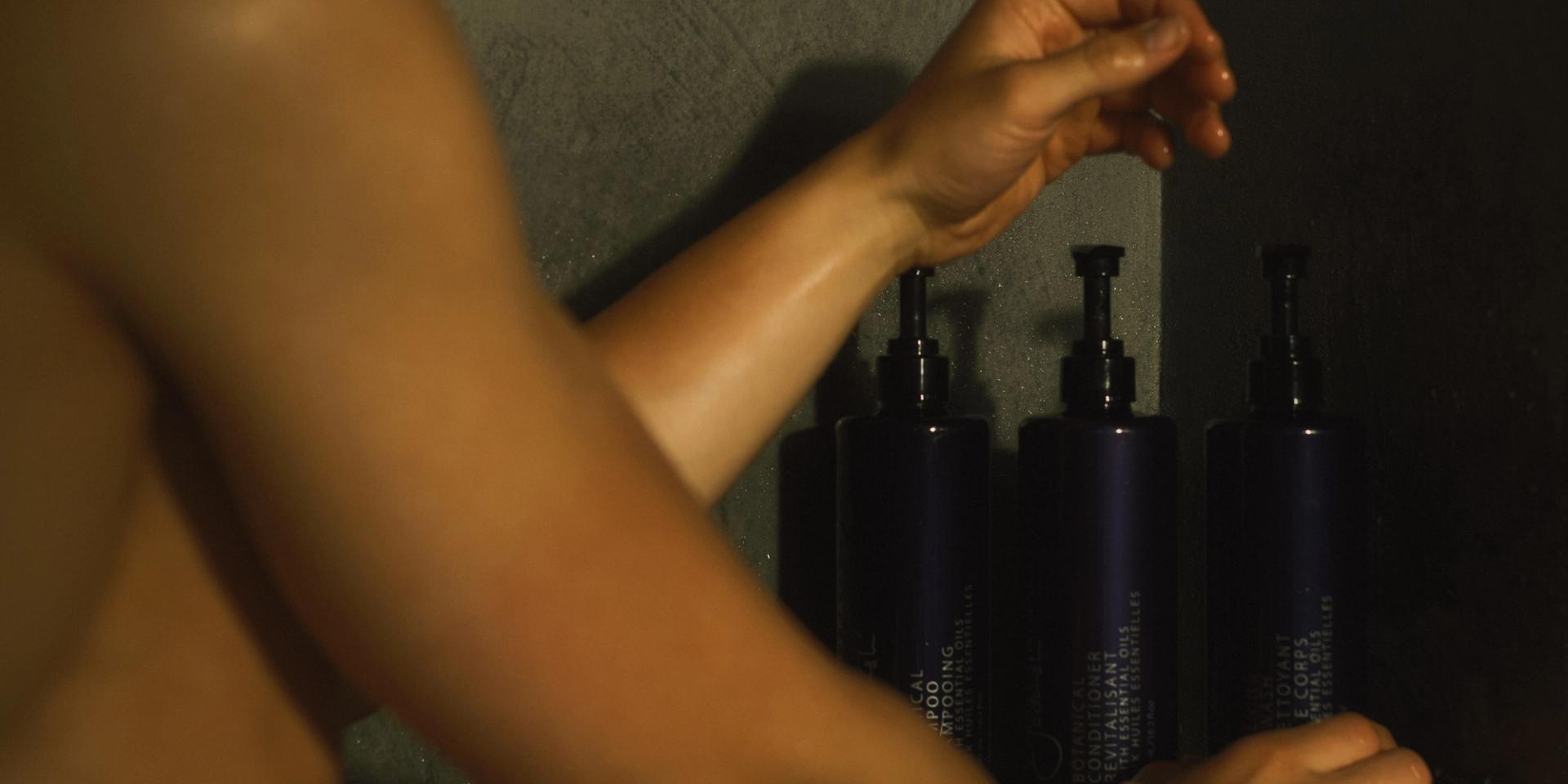 Man in shower grabbing Sodashi Body Wash dispenser on shower shelf