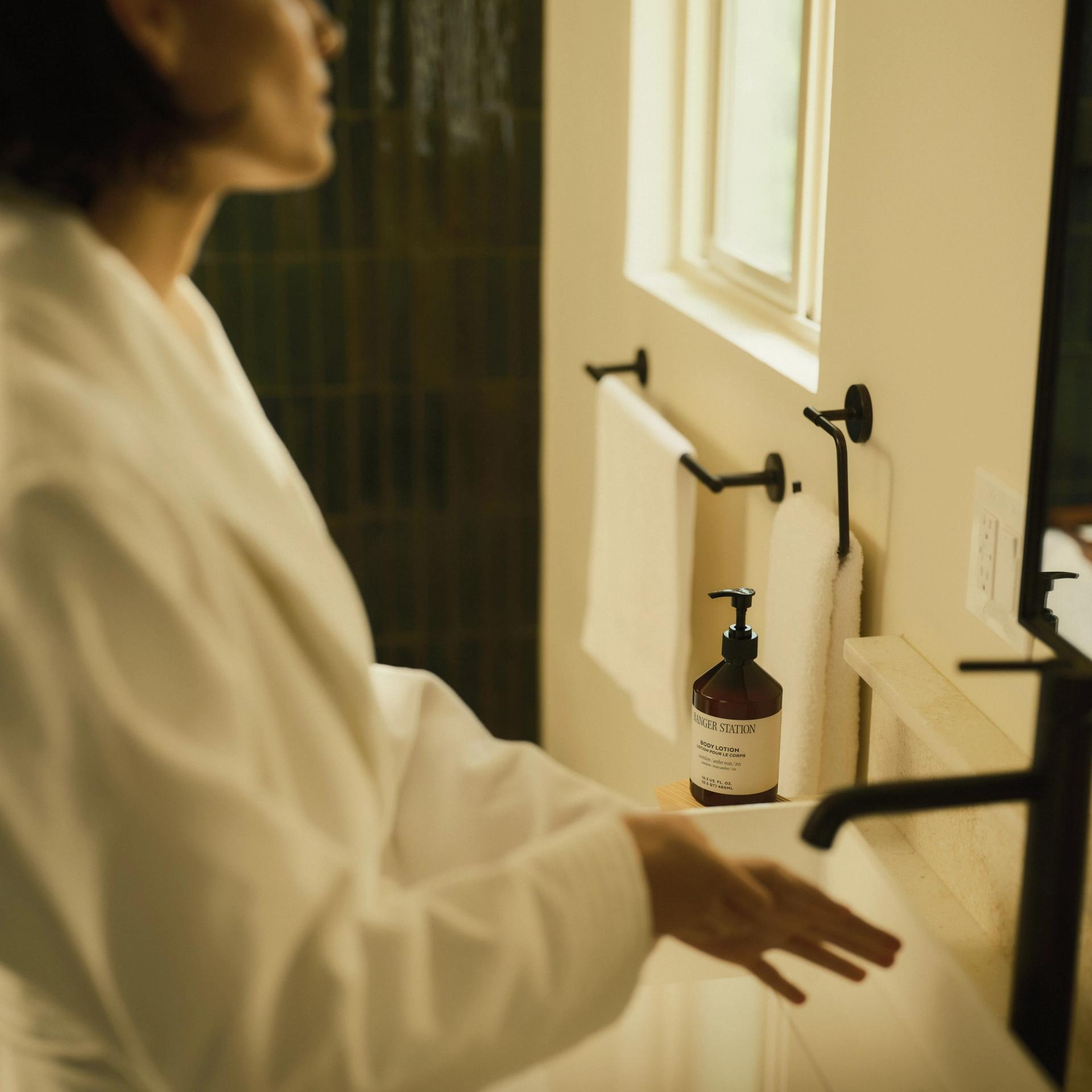 Woman washing hands with Ranger Station Santalum Body Lotion sitting on bathroom vanity counter