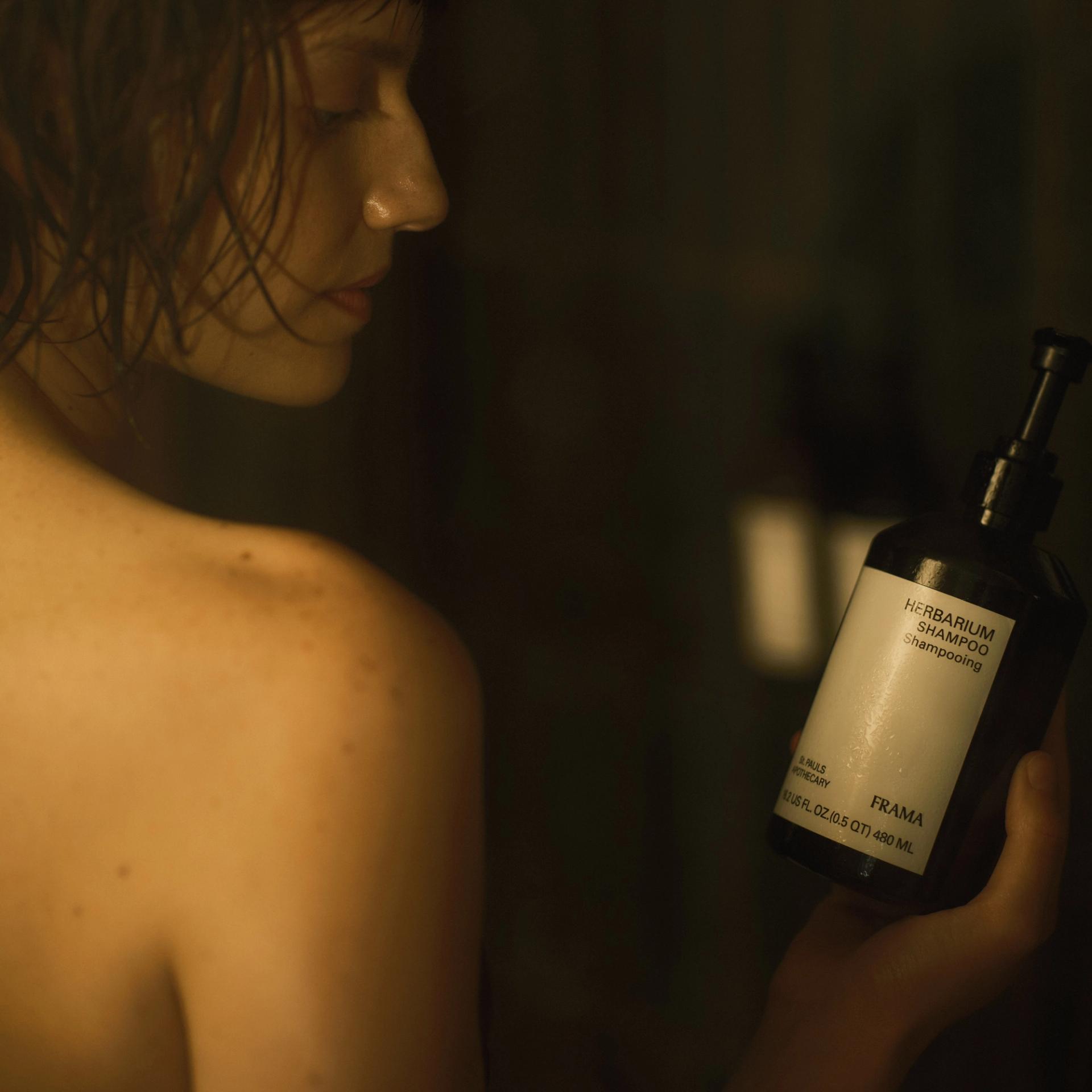 Girl holding bottle of Frama Herbarium Shampoo in the shower