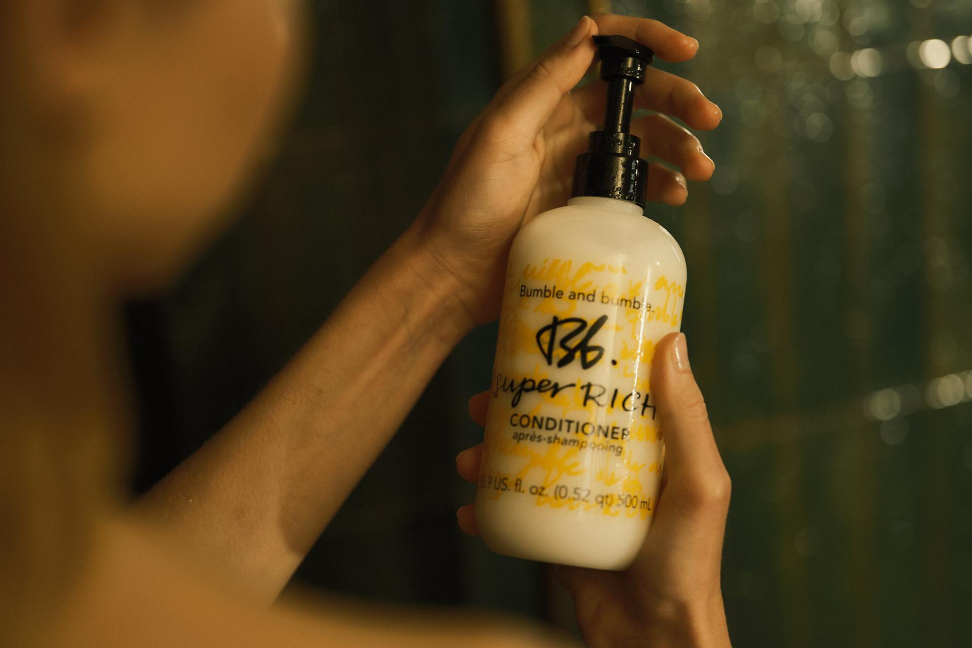 Girl holding a bottle of Bumble & Bumble Conditioner in the shower