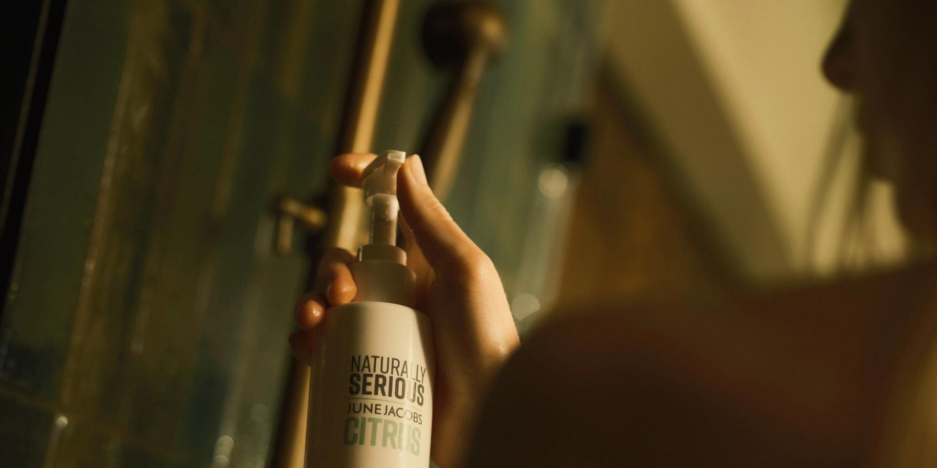 Woman in shower holding Naturally Serious Skincare Body Wash dispenser in hands