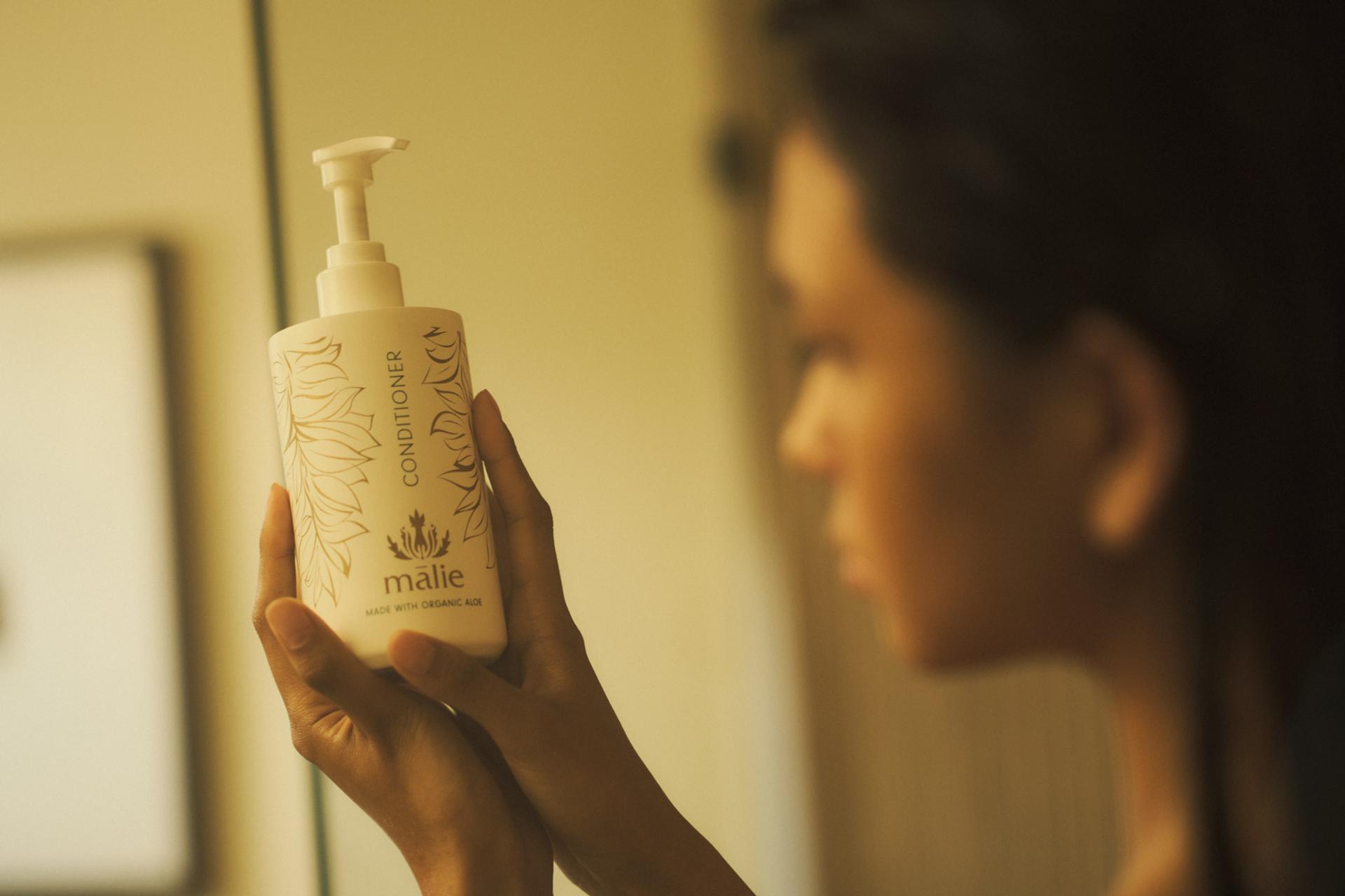 Woman in shower holding Malie Koke'e Conditioner dispenser in hands