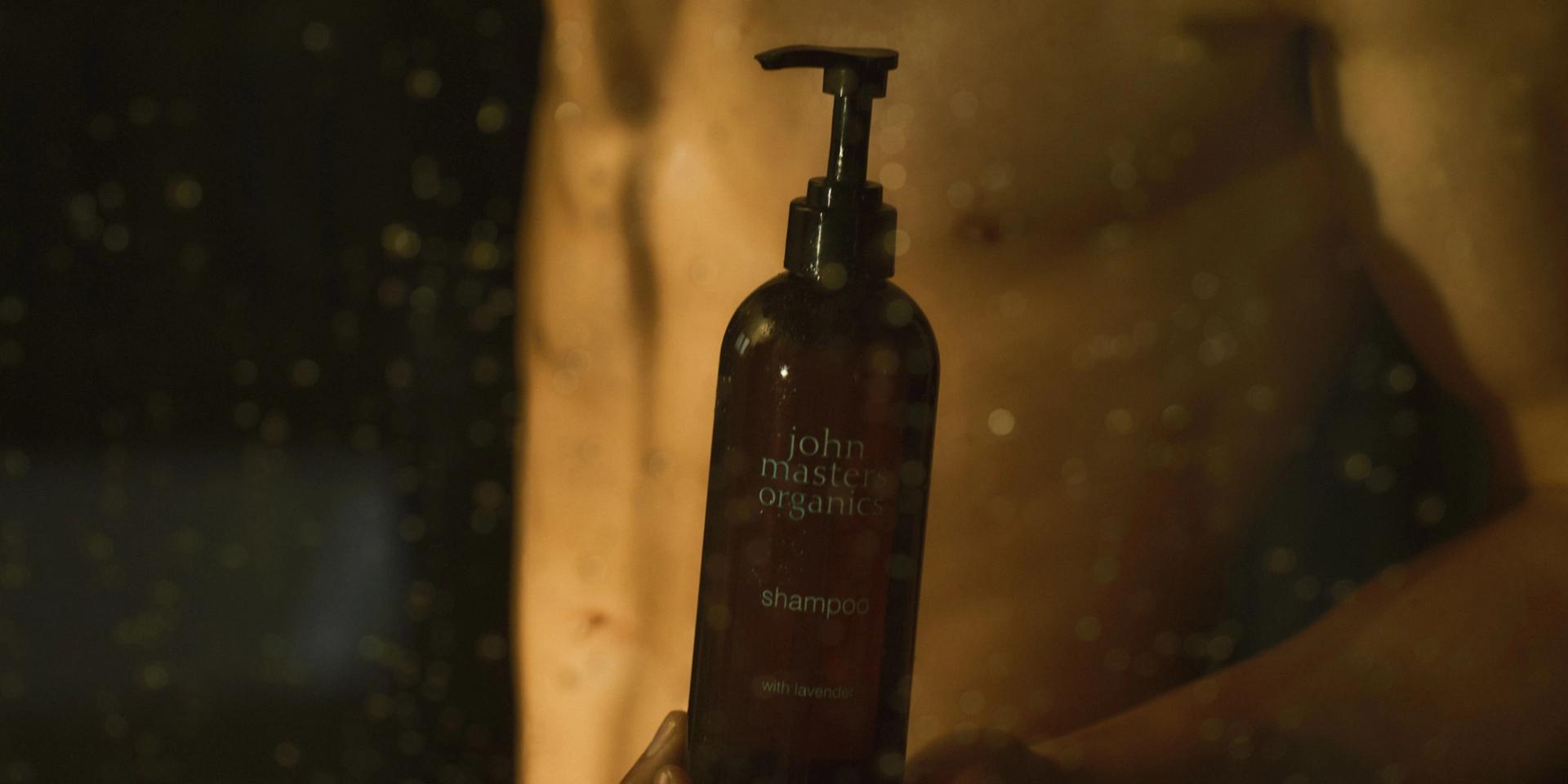 Guy in shower holding a John Masters Organics Shampoo bottle