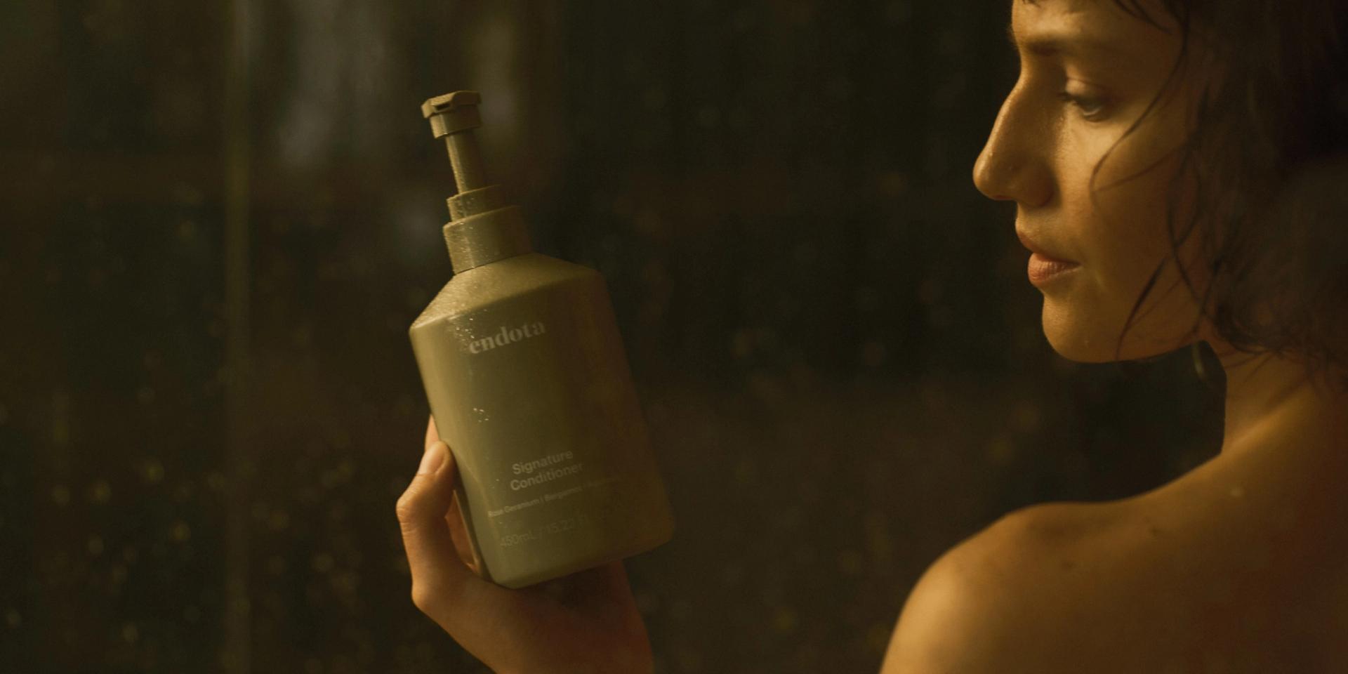 Girl in Shower holding a bottle of endota Signature Conditioner