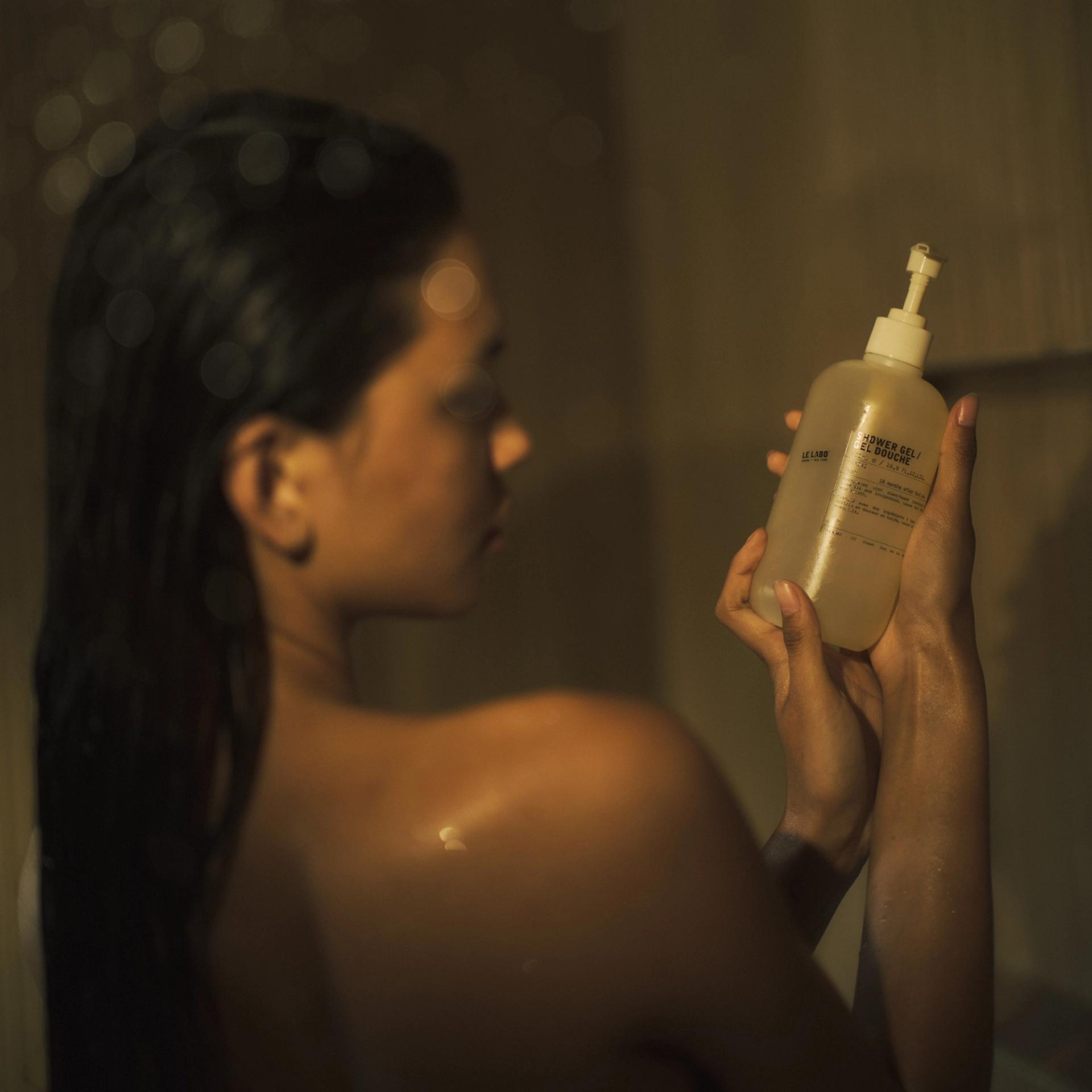 Woman in shower holding Le Labo Hinoki Shower Gel dispenser in hands