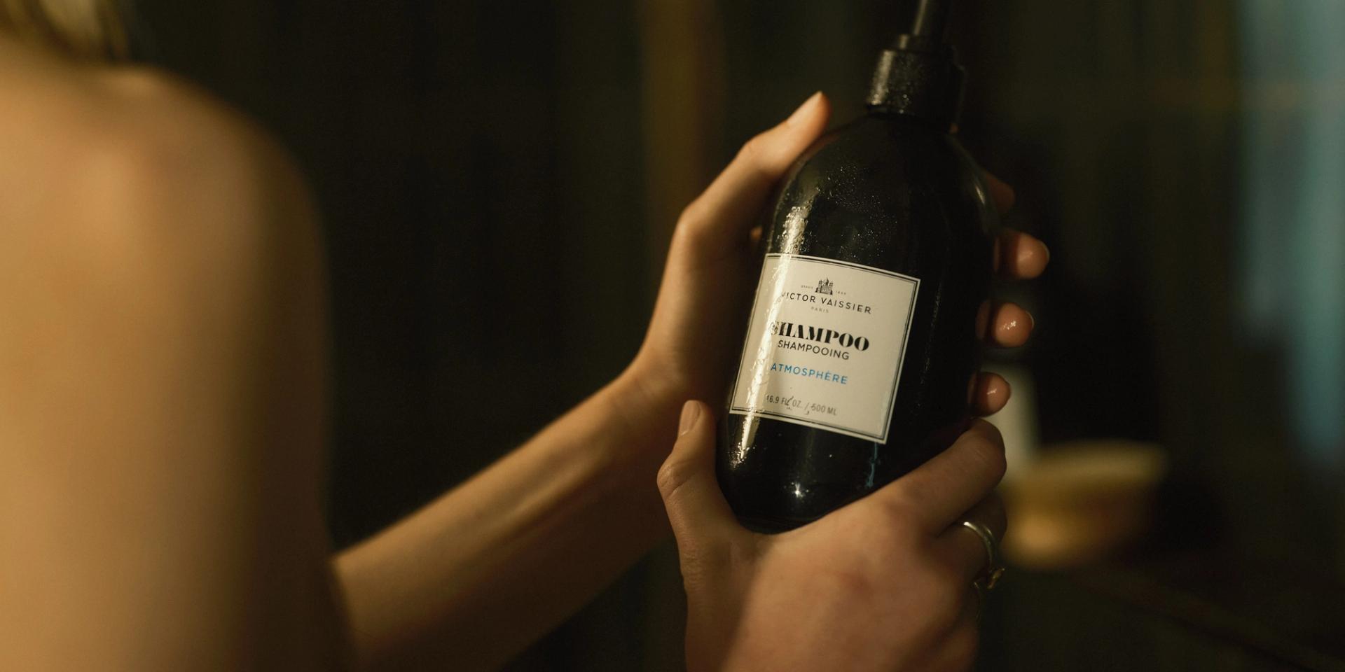 Woman in shower holding Victor Vaissier Shampoo dispenser in hands