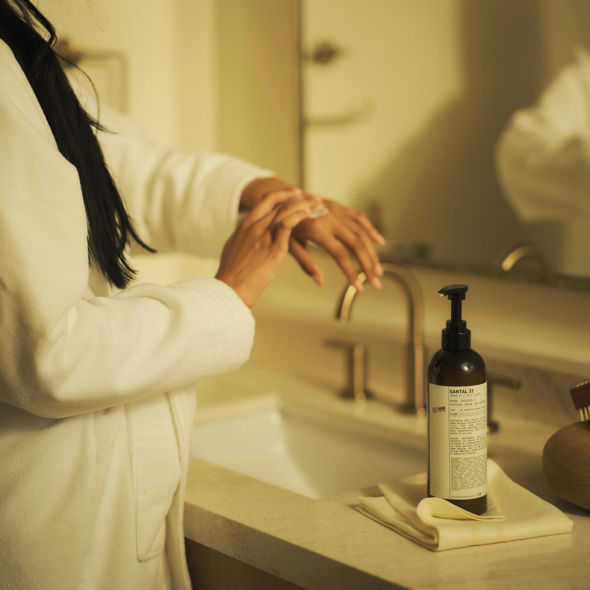 Woman in bathroom applying Le Labo Santal 33 Body Lotion on hands