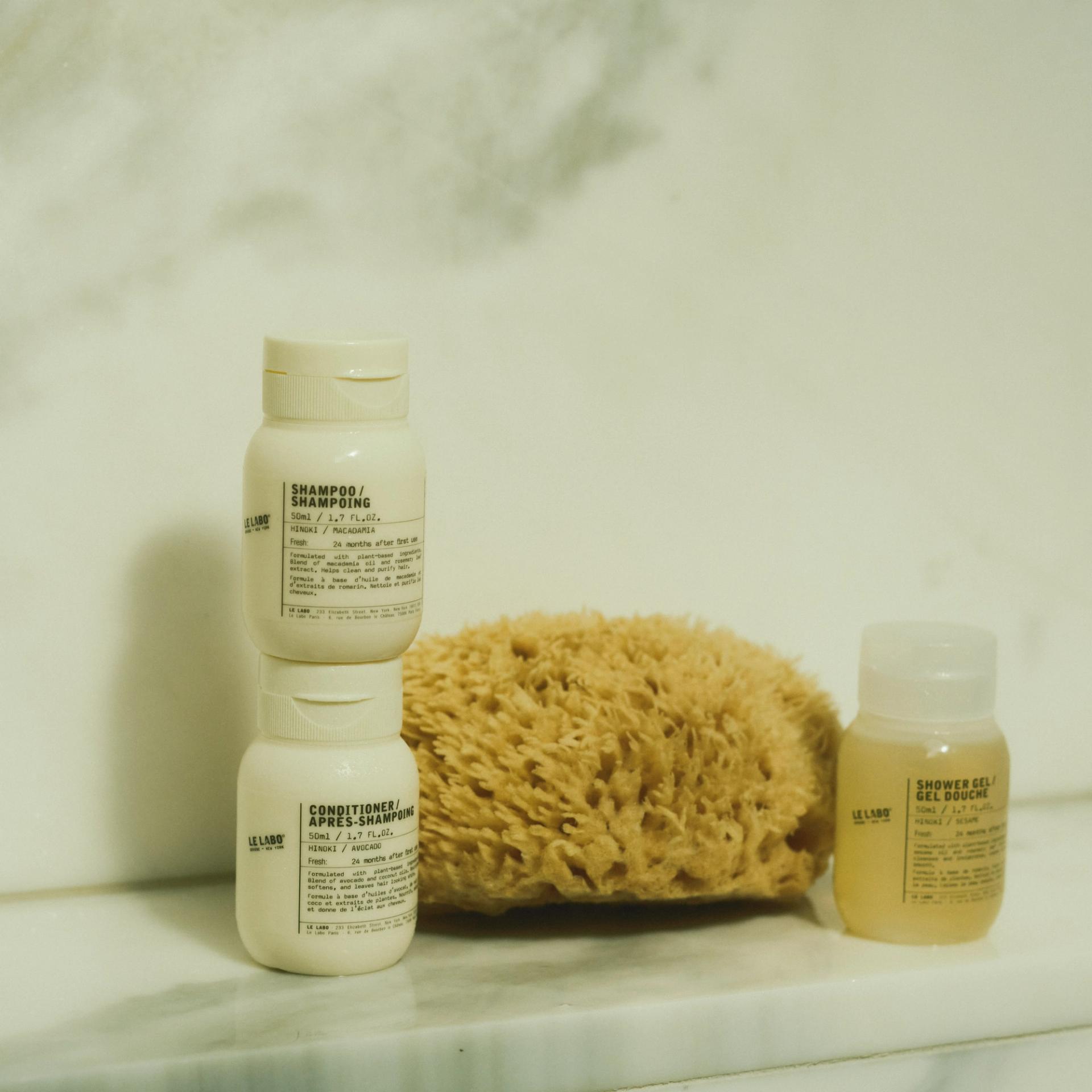 Le Labo Hinoki Shampoo, Conditioner and Shower Gel single-use amenities on marble shower shelf
