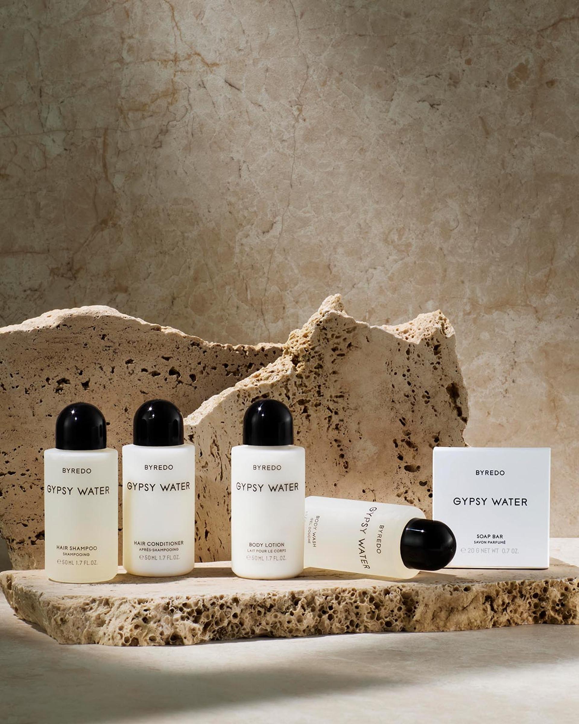 Byredo Gypsy Water Small Format Shampoo, Conditioner, Body Lotion, Body Wash and boxed Soap Bar sitting on rock
