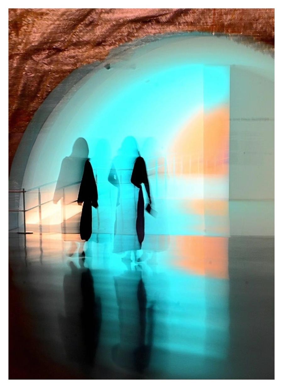 Two blurred figures walking through a glowing teal archway, their reflections on a polished floor