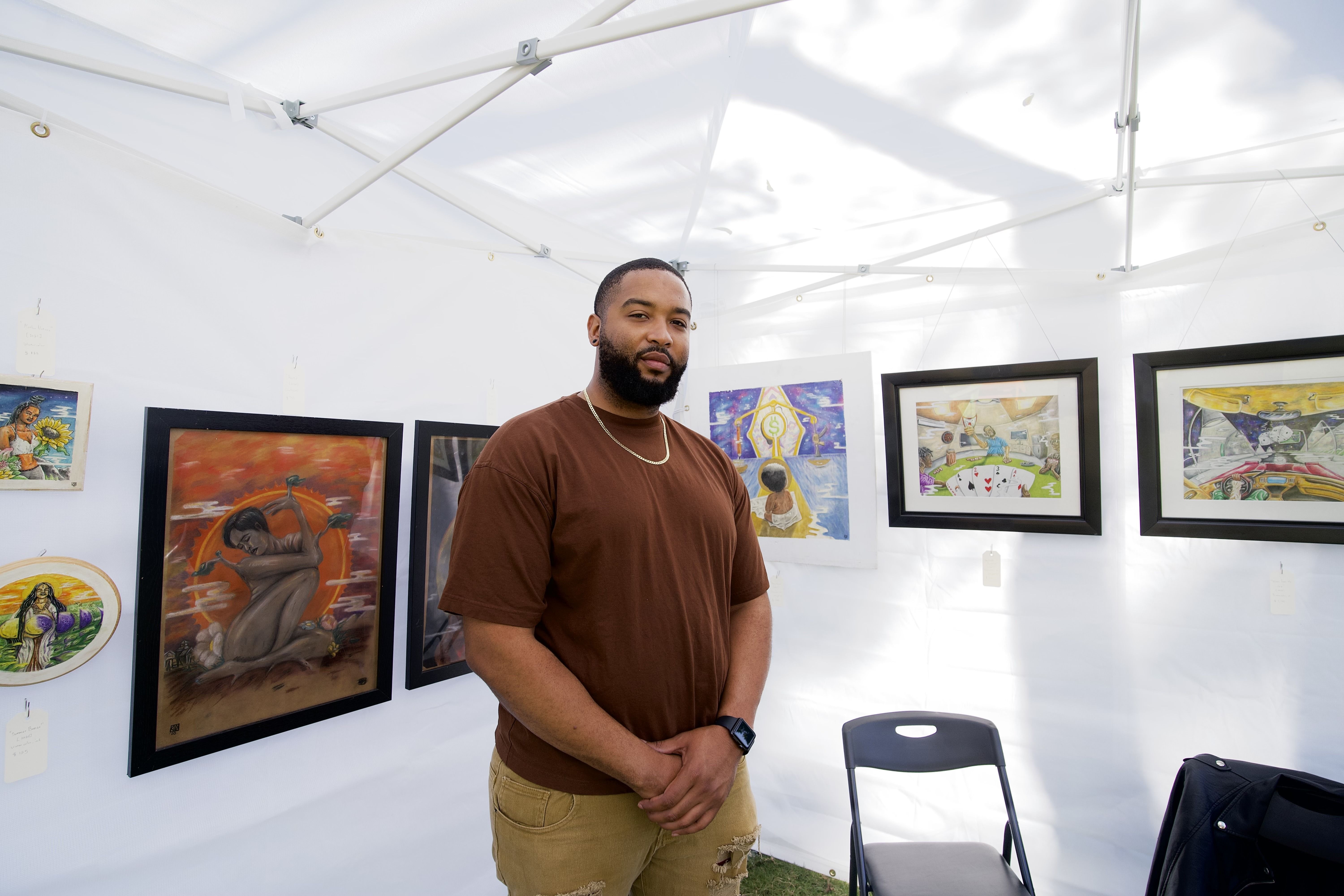 Darrell Robins standing in a white art-fair tent, framed paintings and drawings hung on the walls around the tent