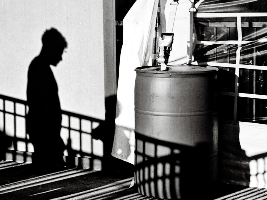 People of the Dark: black-and-white shadow of a man cast on a wall beside a railing and a barrel