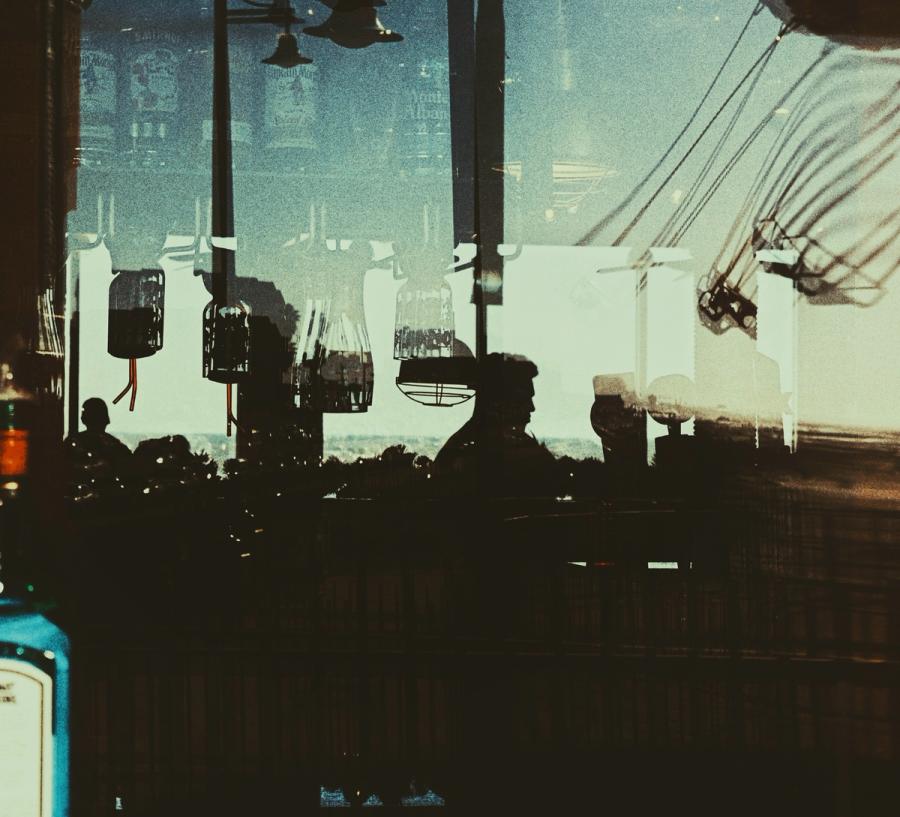 Layered reflections in glass: silhouettes of diners, hanging lights and a swing ride in green and amber tones