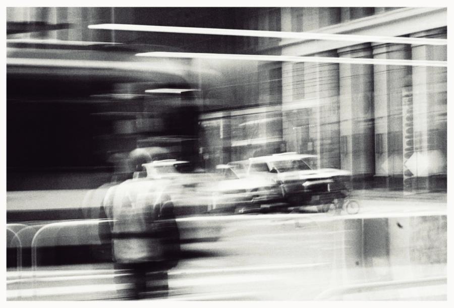 Rush Hour: black-and-white street scene in motion blur, a person and cars streaking past a building