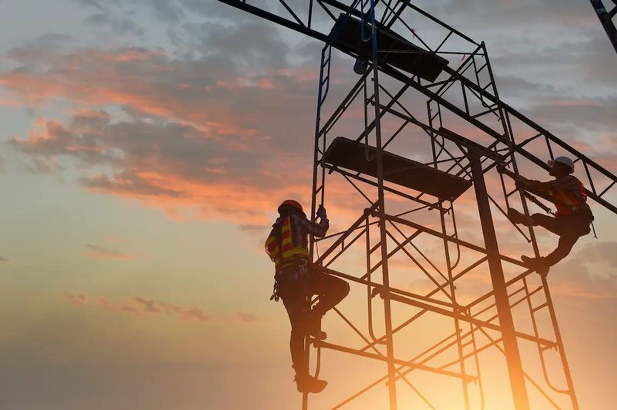 Two construction workers climbing a scaffolding during sunset