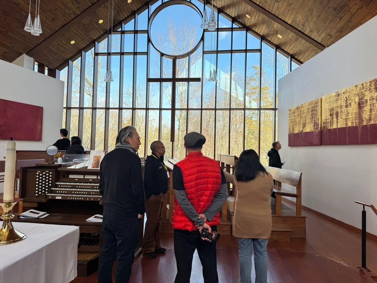 A small group of people standing still in a church, appreciating the gilded artwork of Mako Fujimura displayed