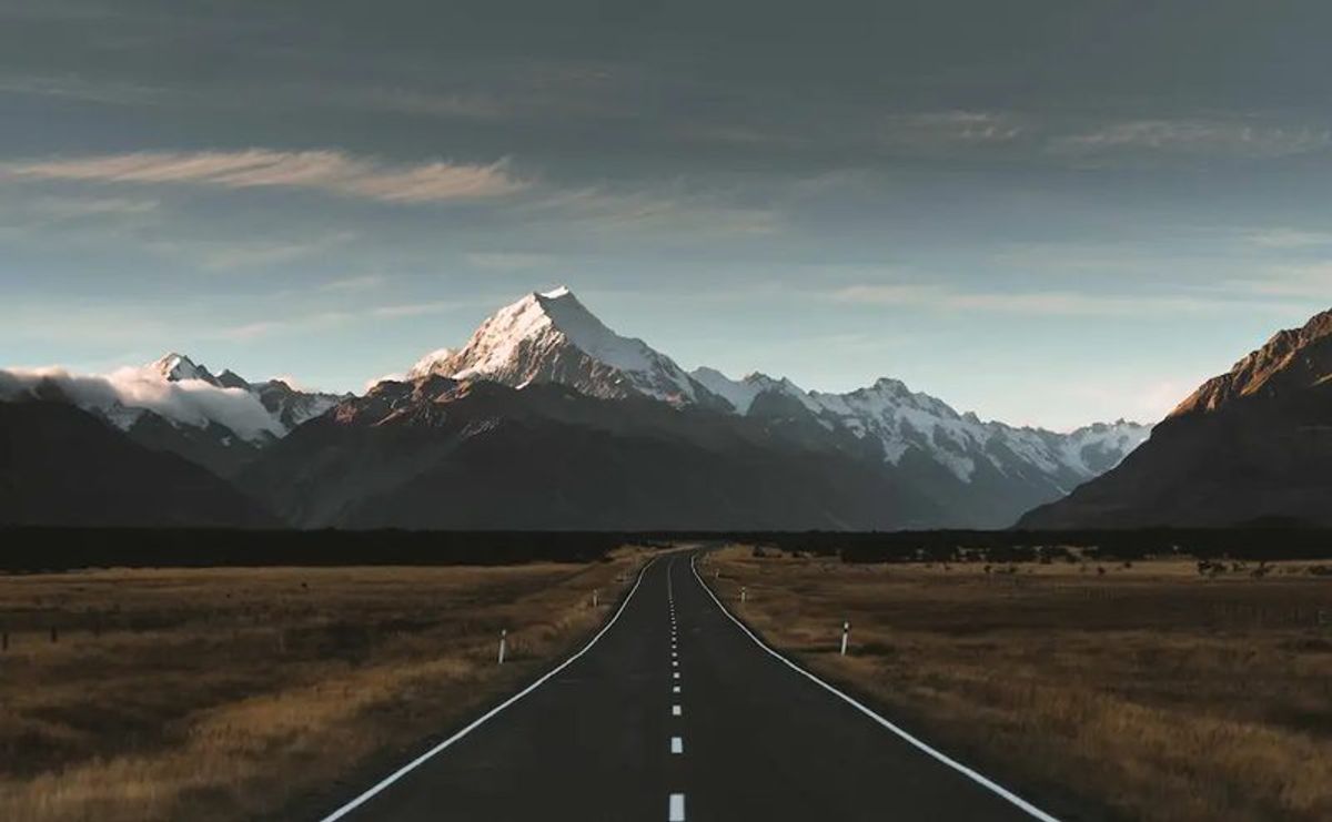 Gray concrete road near mountain under cloudy sky