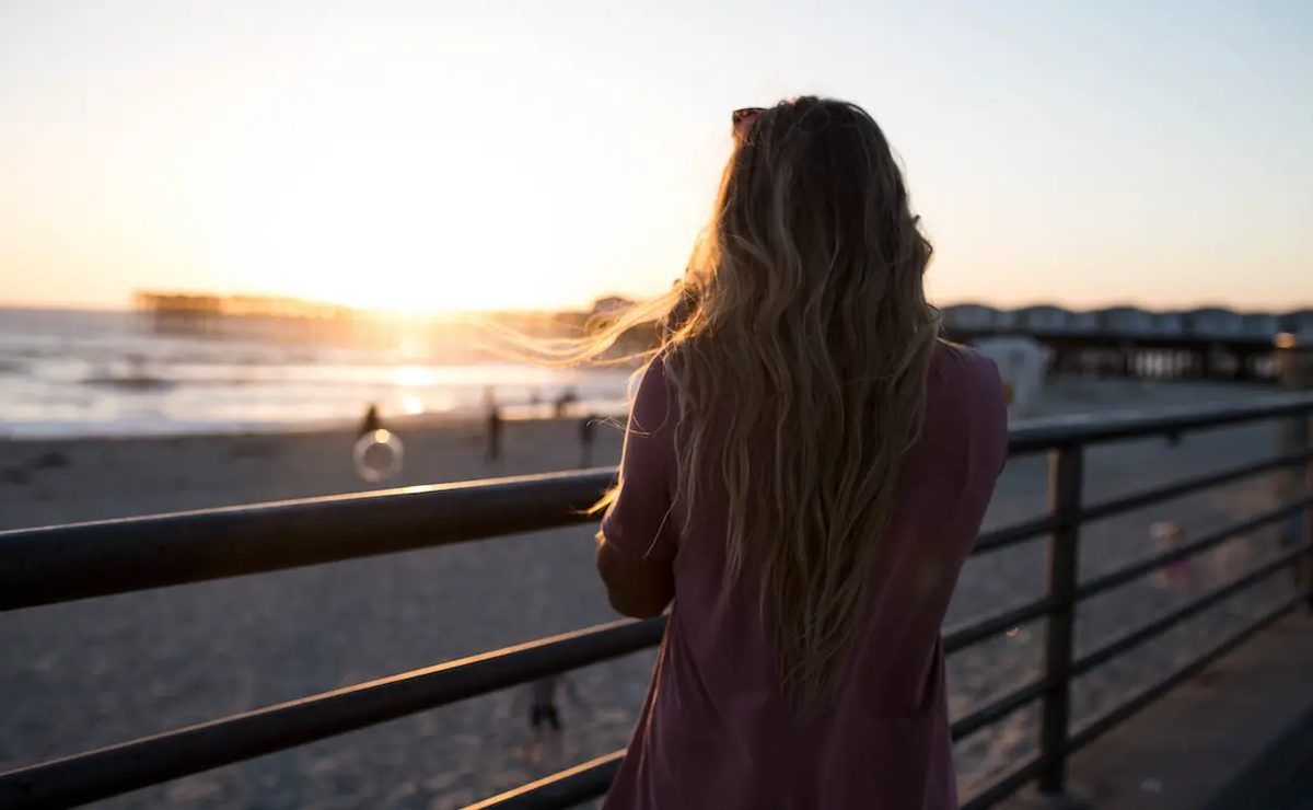 Woman in brown dress standing near railings during sunset