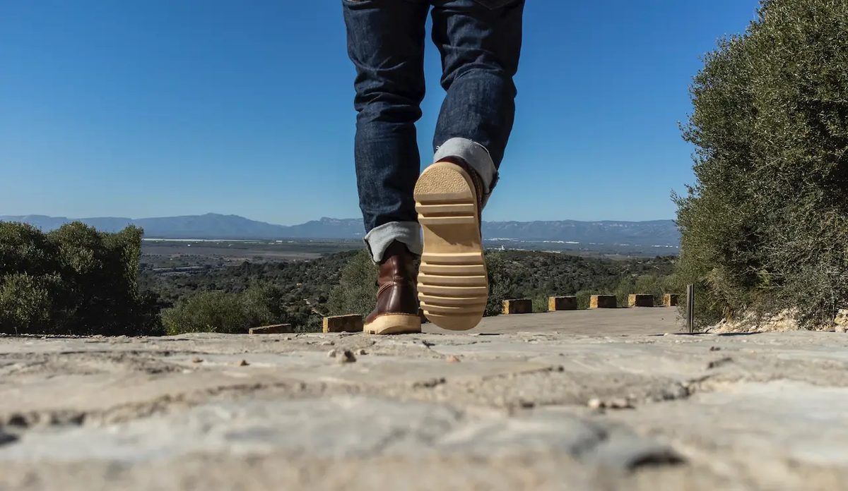 Person in blue denim jeans and brown shoes standing on brown dirt ground