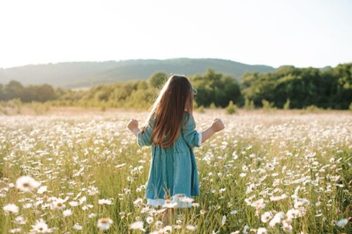 girl in field, playing in flowers with back toward camera