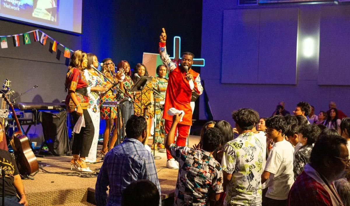 Vibrantly dressed people on stage leading immigrant church