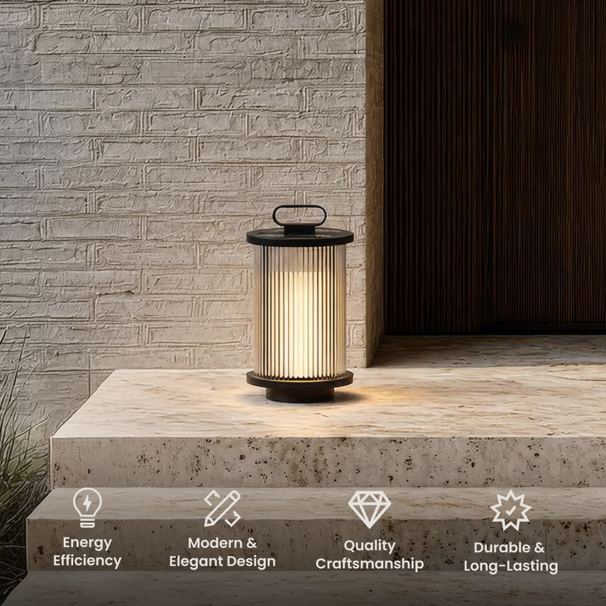 Vesper black portable lantern, ribbed glass cylinder with a top handle, on a stone step by a brick wall