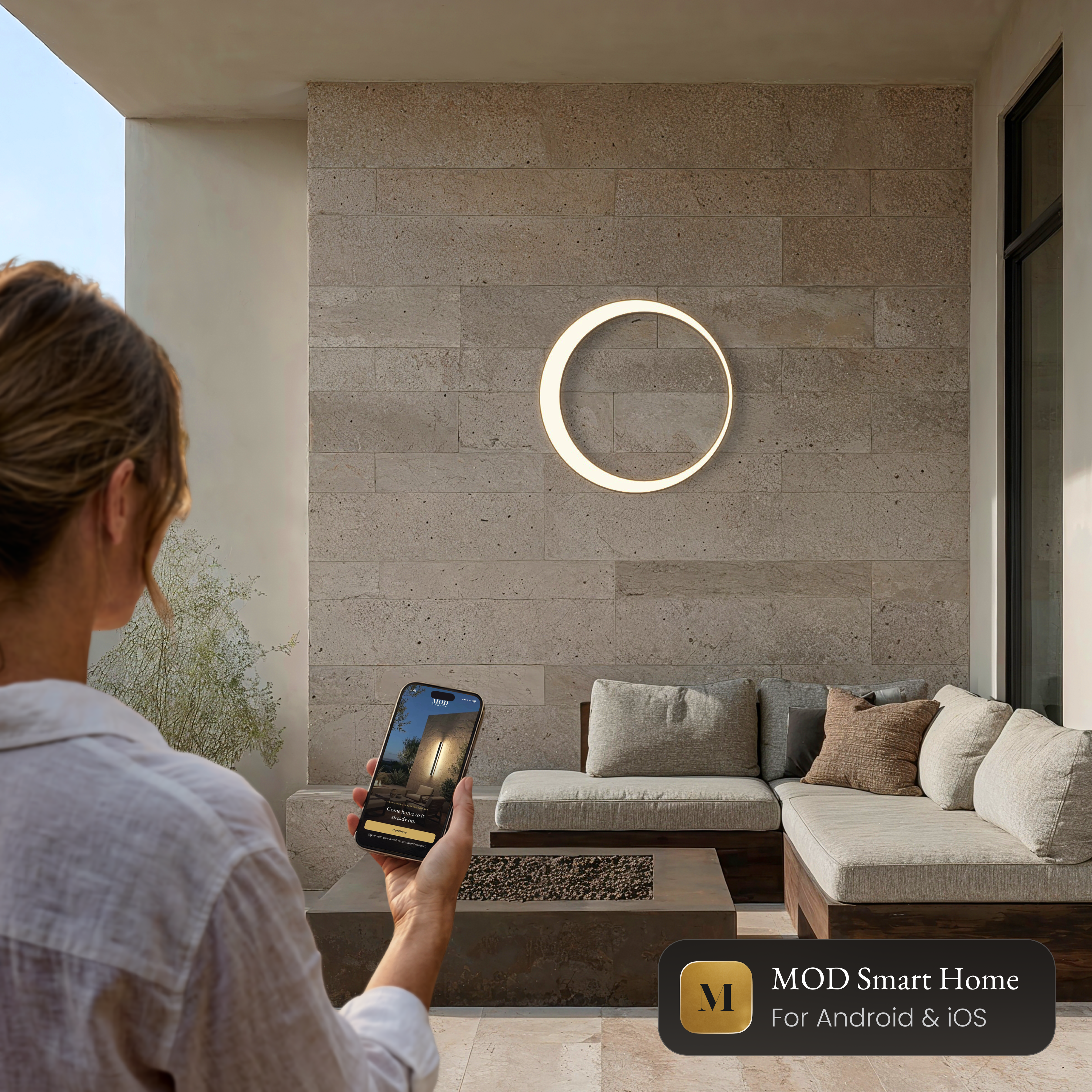 Gleam Smart round LED wall light on a stone wall, controlled from the MOD Smart Home app on a phone