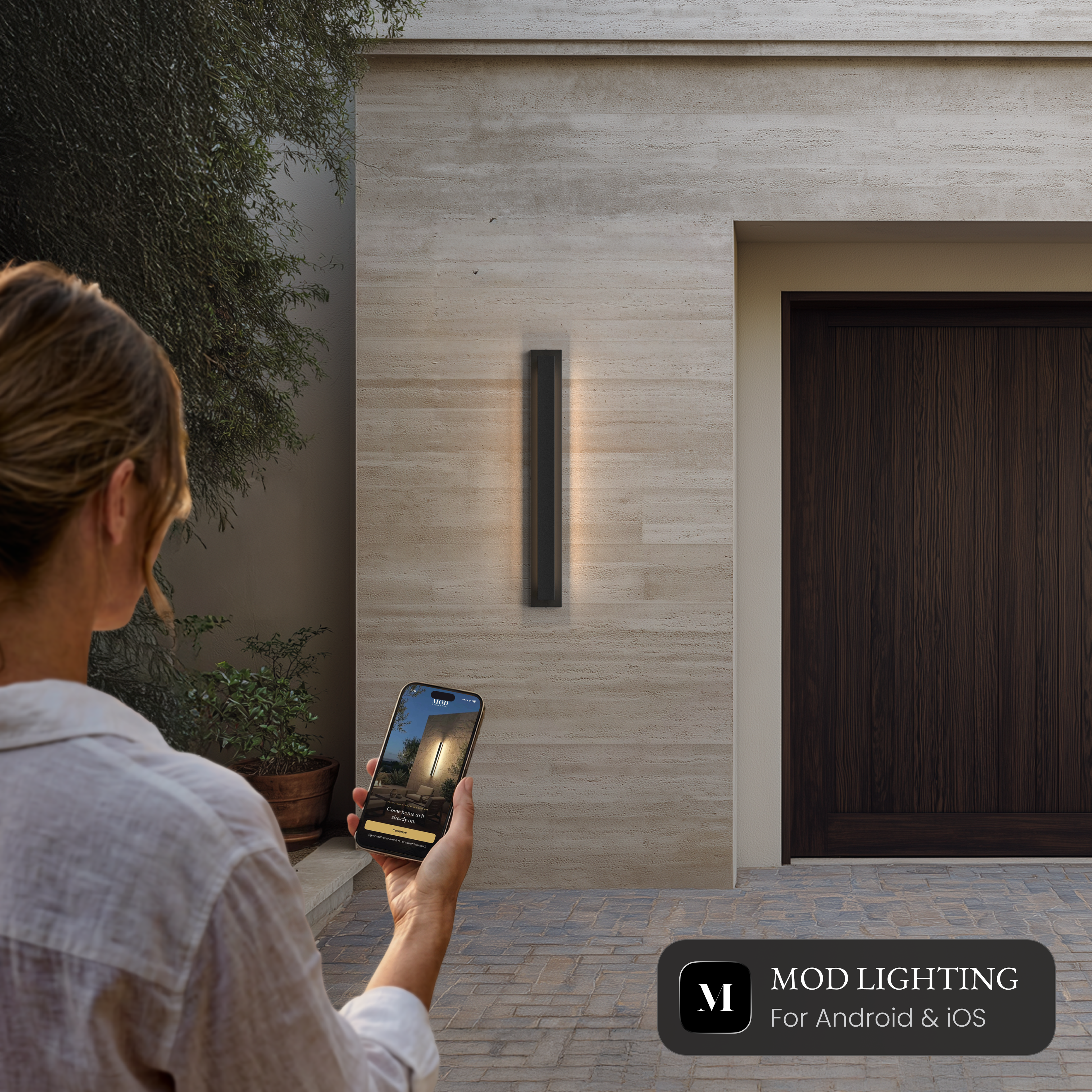 Vetra Smart black vertical LED sconce on a stone wall, controlled from the MOD LIGHTING app on a phone