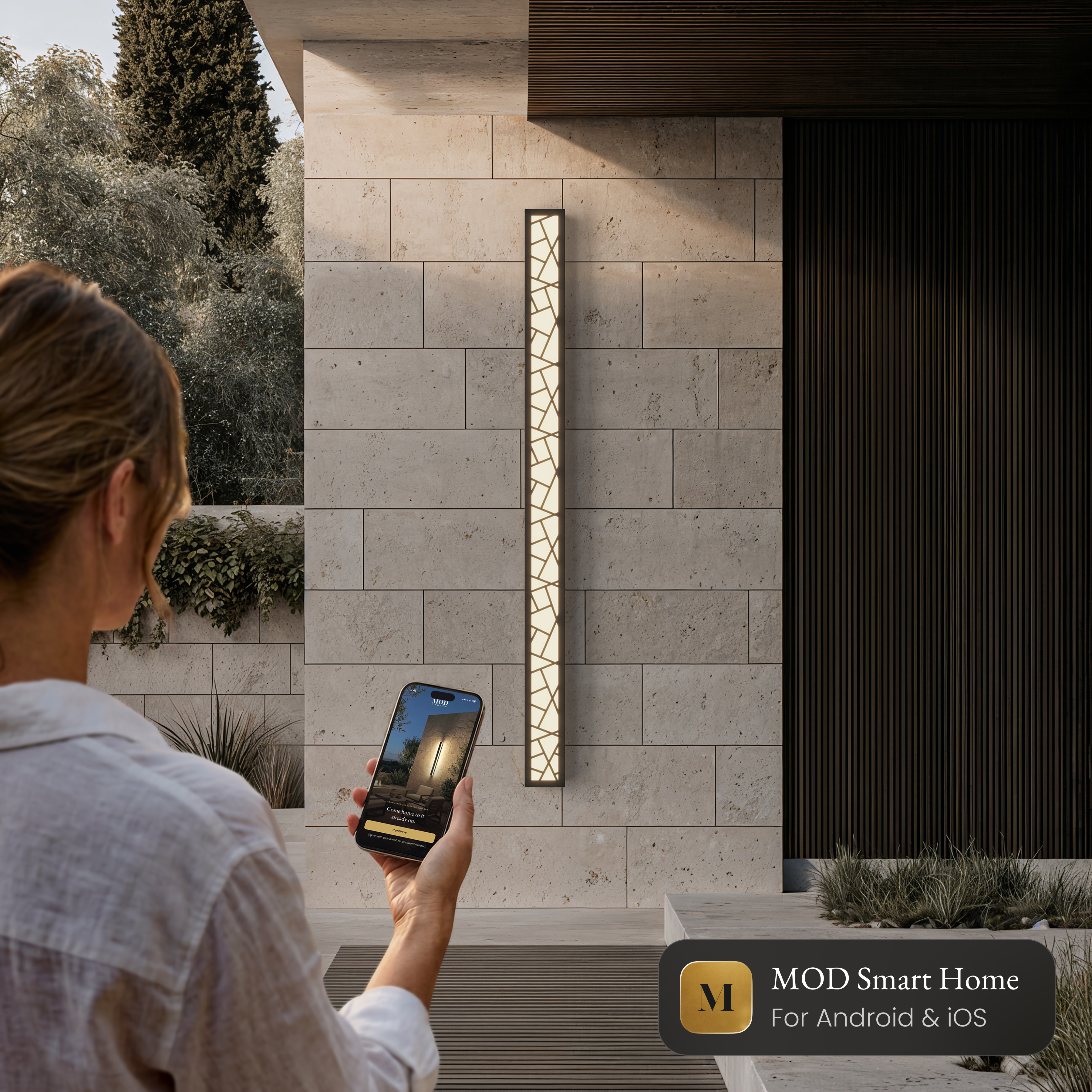 Harper Smart black LED bar wall light on a stone wall, controlled from the MOD Smart Home app on a phone