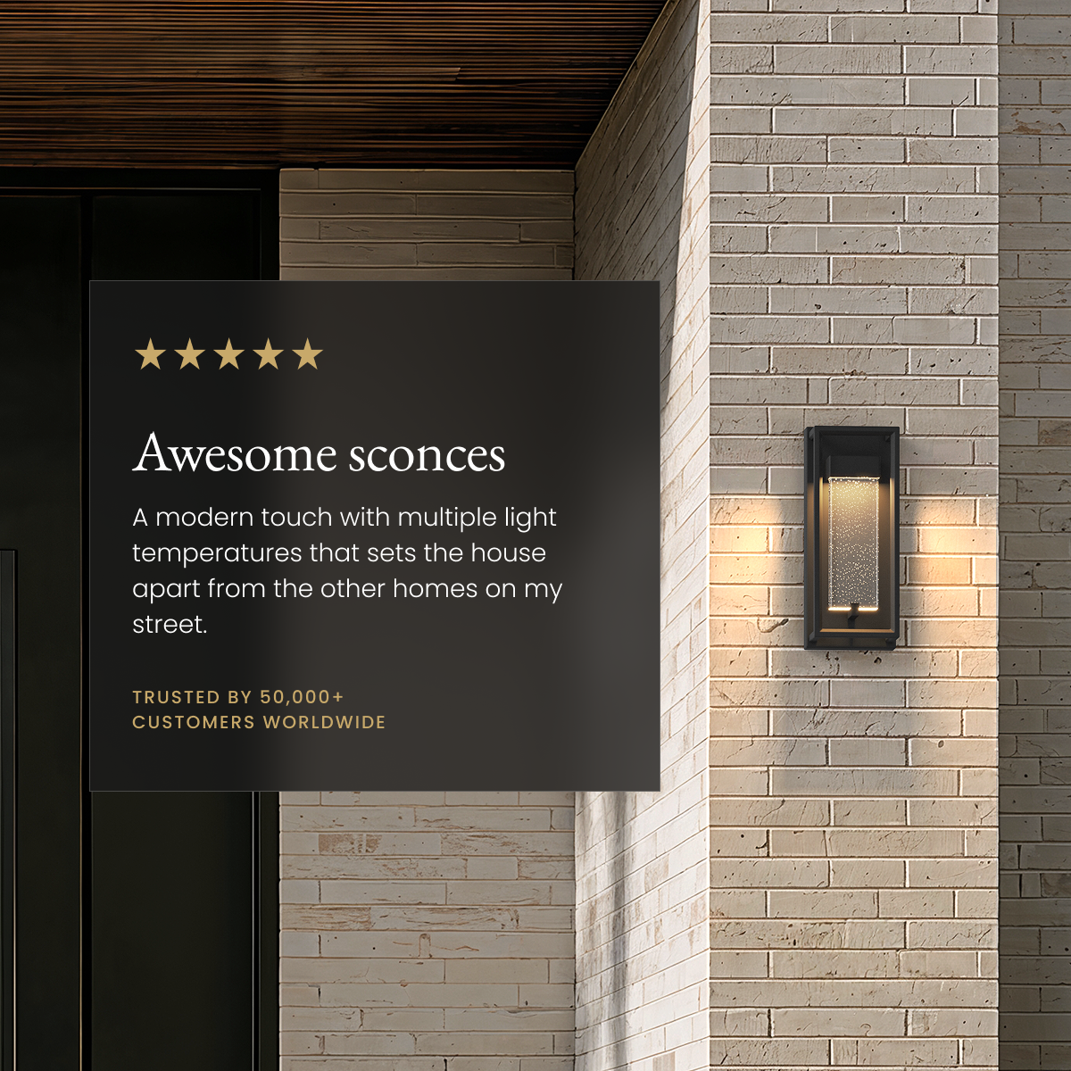 Aura black outdoor sconce, open frame with seeded-glass core glowing on a stone-brick facade beside a review card