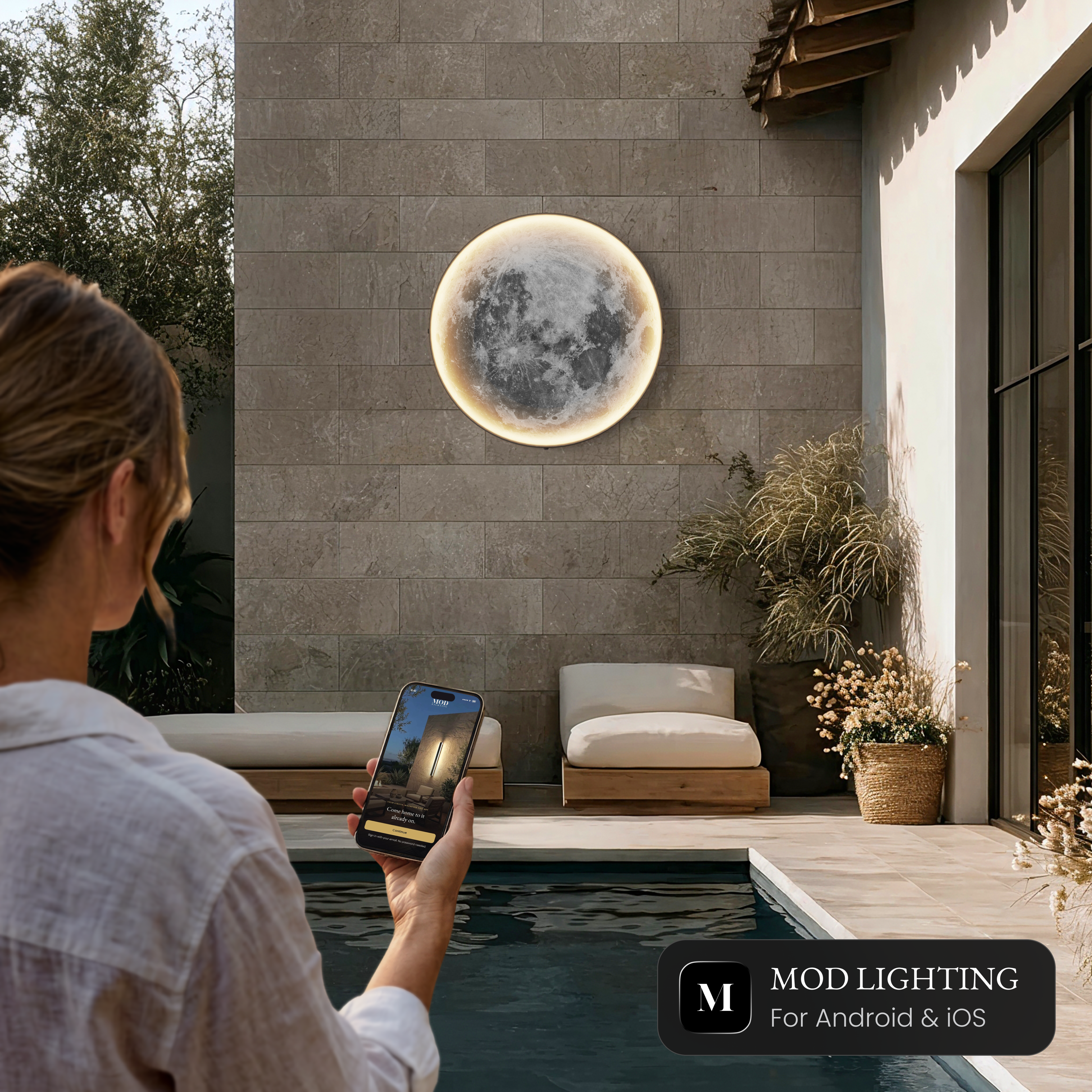 Luna Outdoor Smart moon wall light beside a pool, controlled from the MOD LIGHTING app on a phone