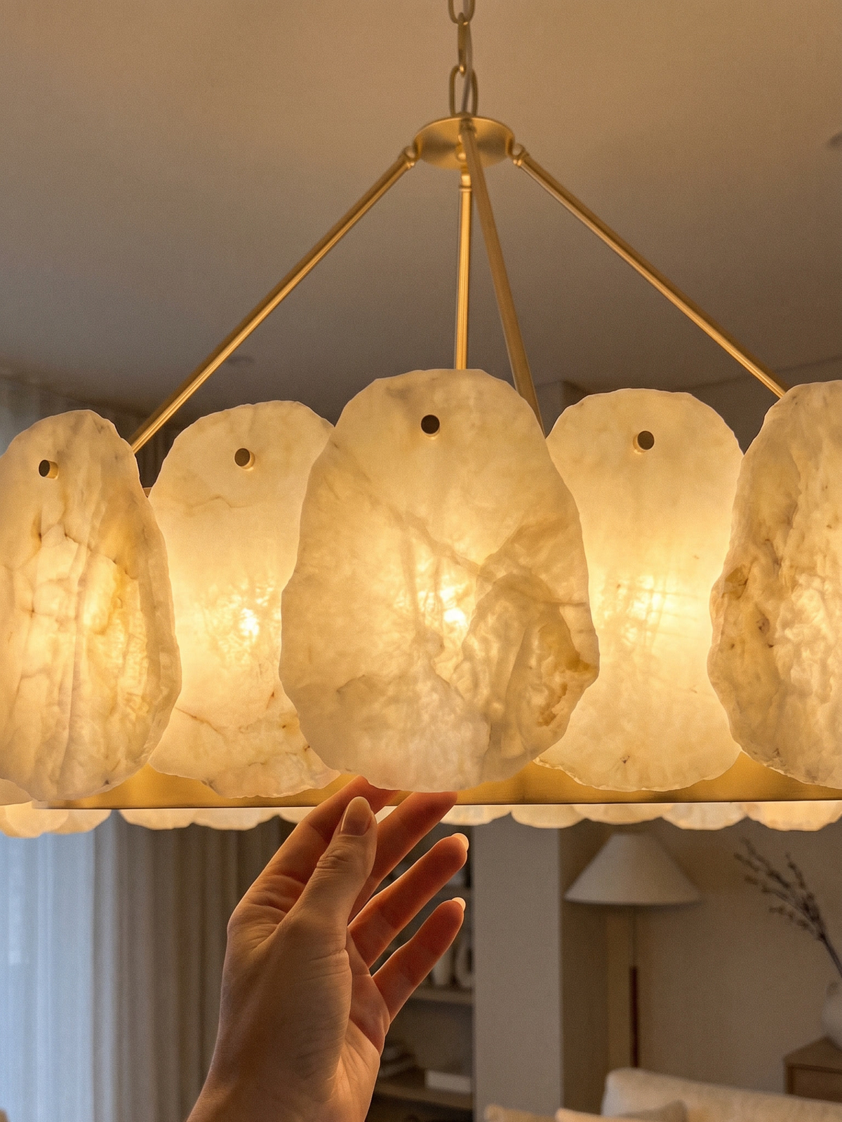 Hand reaching up to the lit alabaster and brass drum of a MOD LIGHTING Alba chandelier