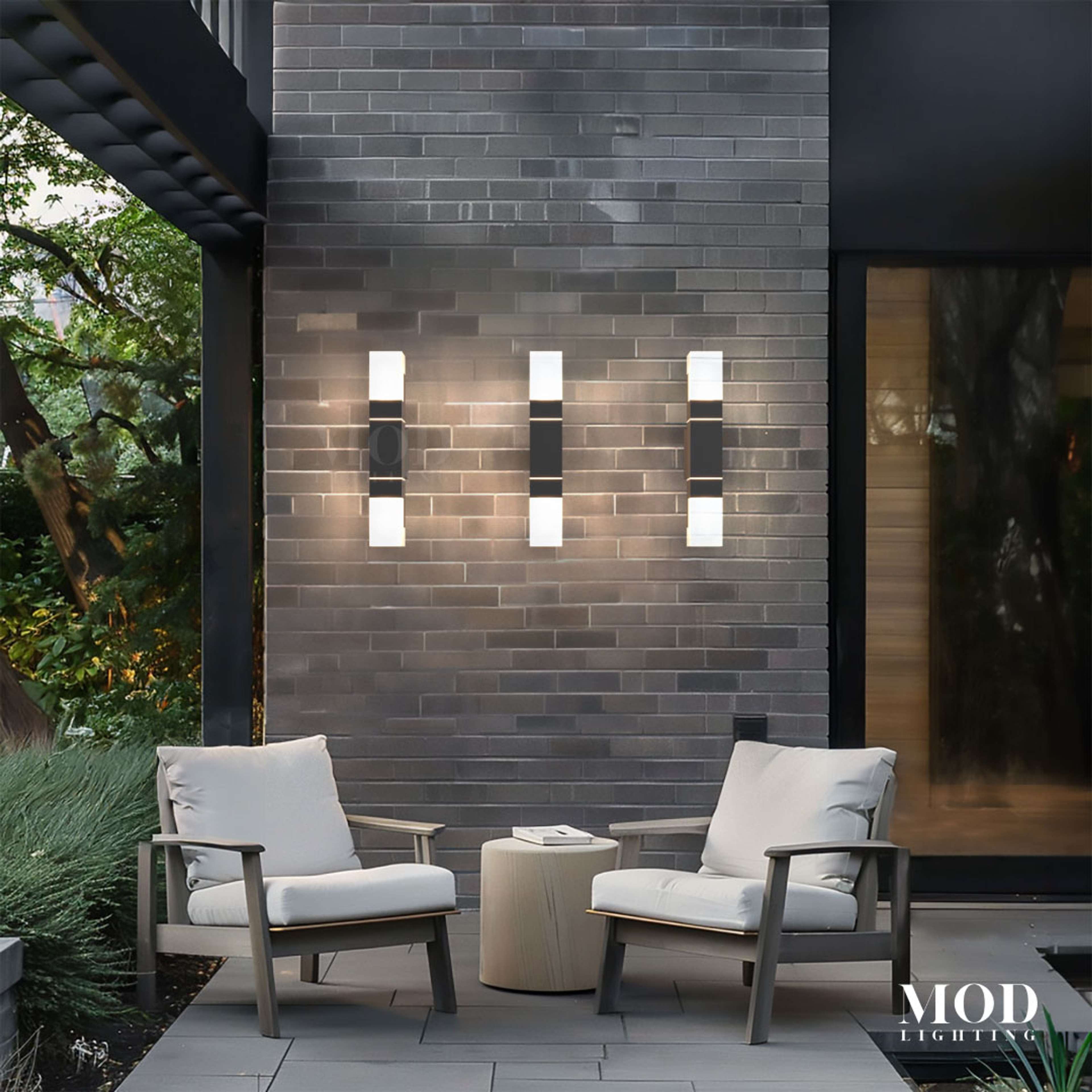 Falcon black outdoor sconces, slim dual-glow bars, three fixtures on a brick patio wall above lounge chairs