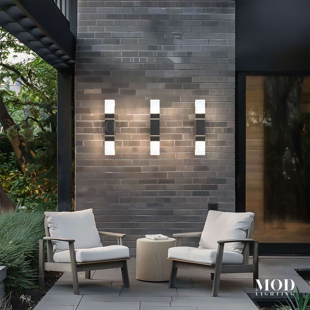 Falcon black outdoor sconces, slim dual-glow bars, three fixtures on a brick patio wall above lounge chairs
