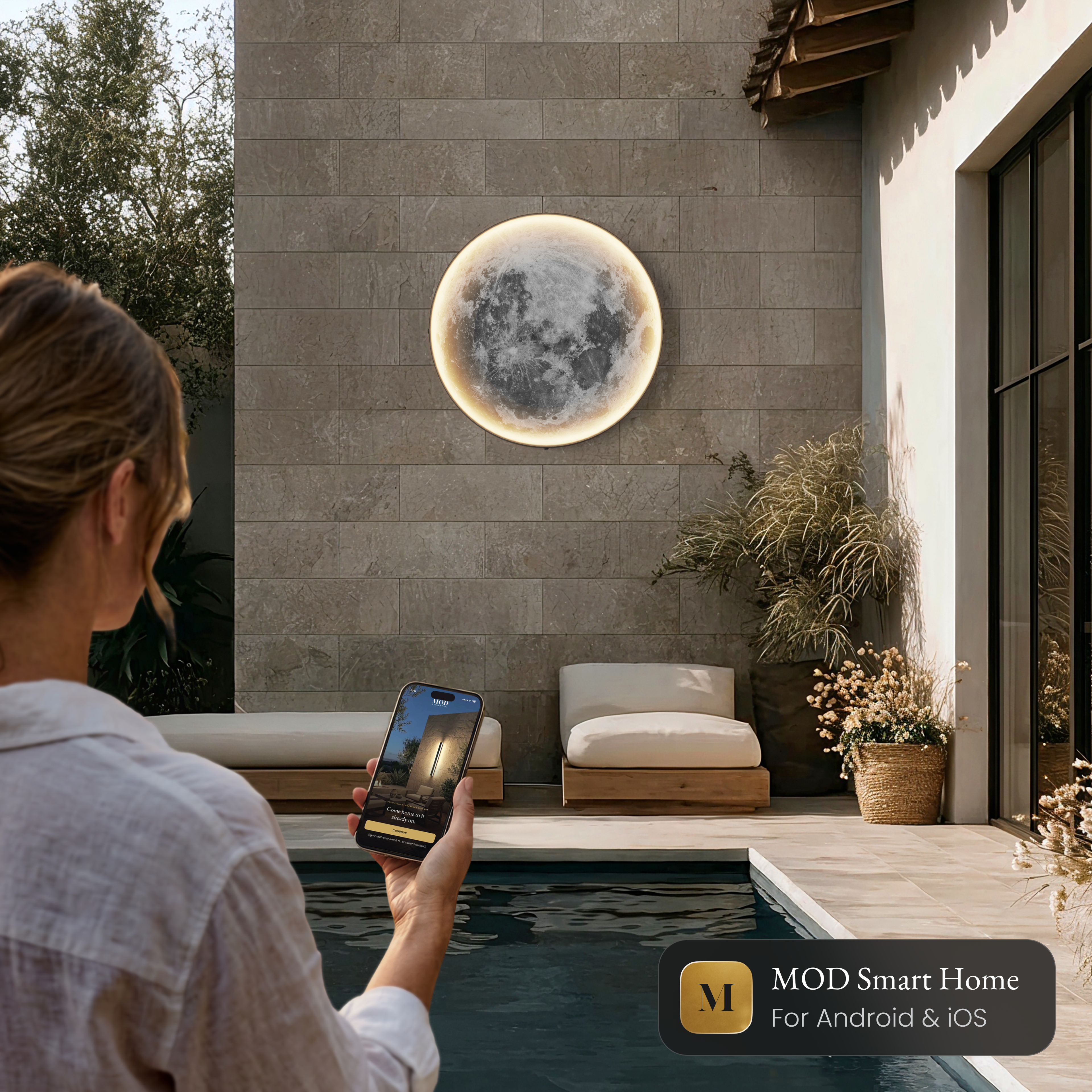 Luna Outdoor Smart moon wall light beside a pool, controlled from the MOD Smart Home app on a phone