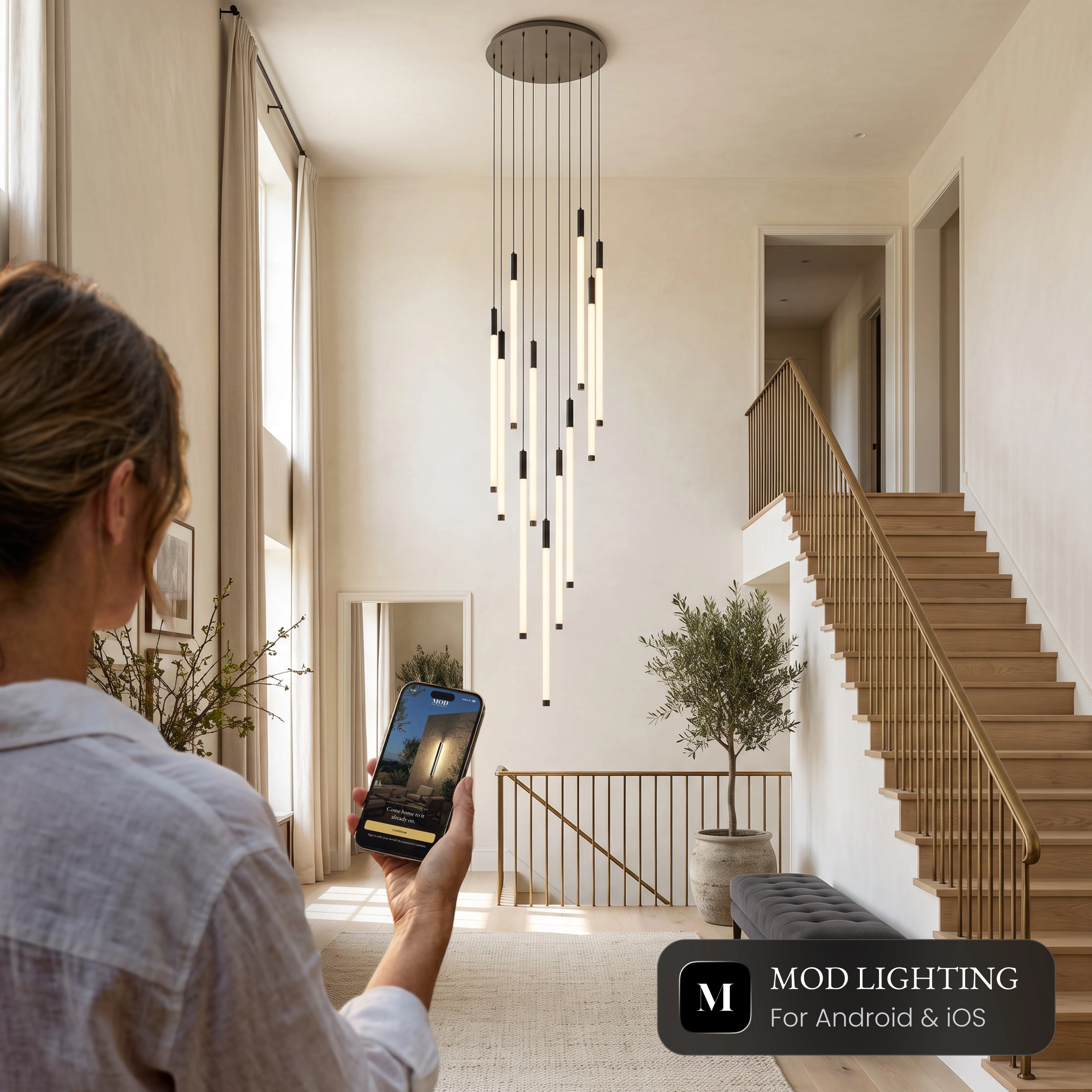 Woman controlling the Kasper Smart staircase chandelier from the MOD Smart Home app on her phone
