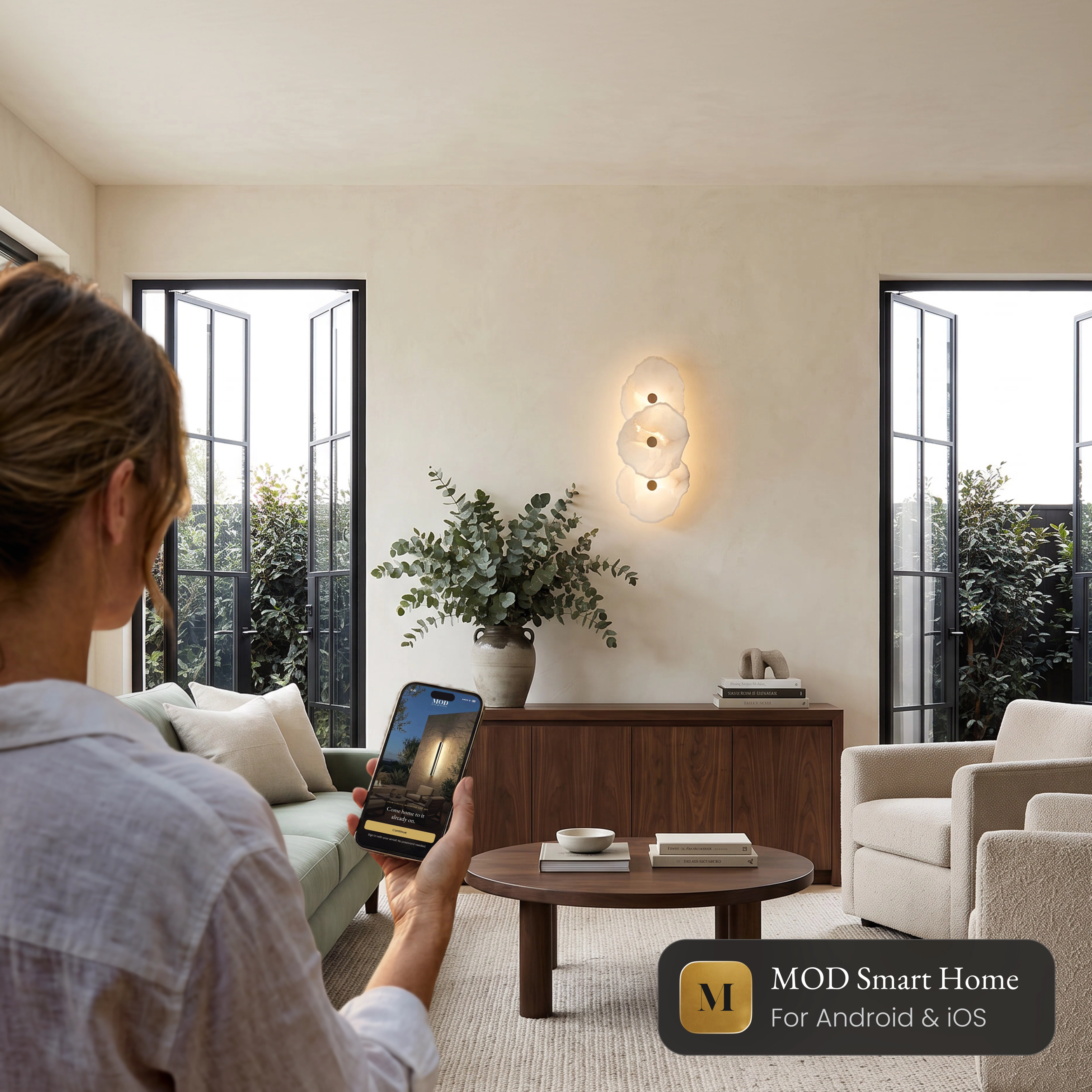 Alba Sconce Smart alabaster wall sconce in a living room, controlled from the MOD Smart Home app on a phone