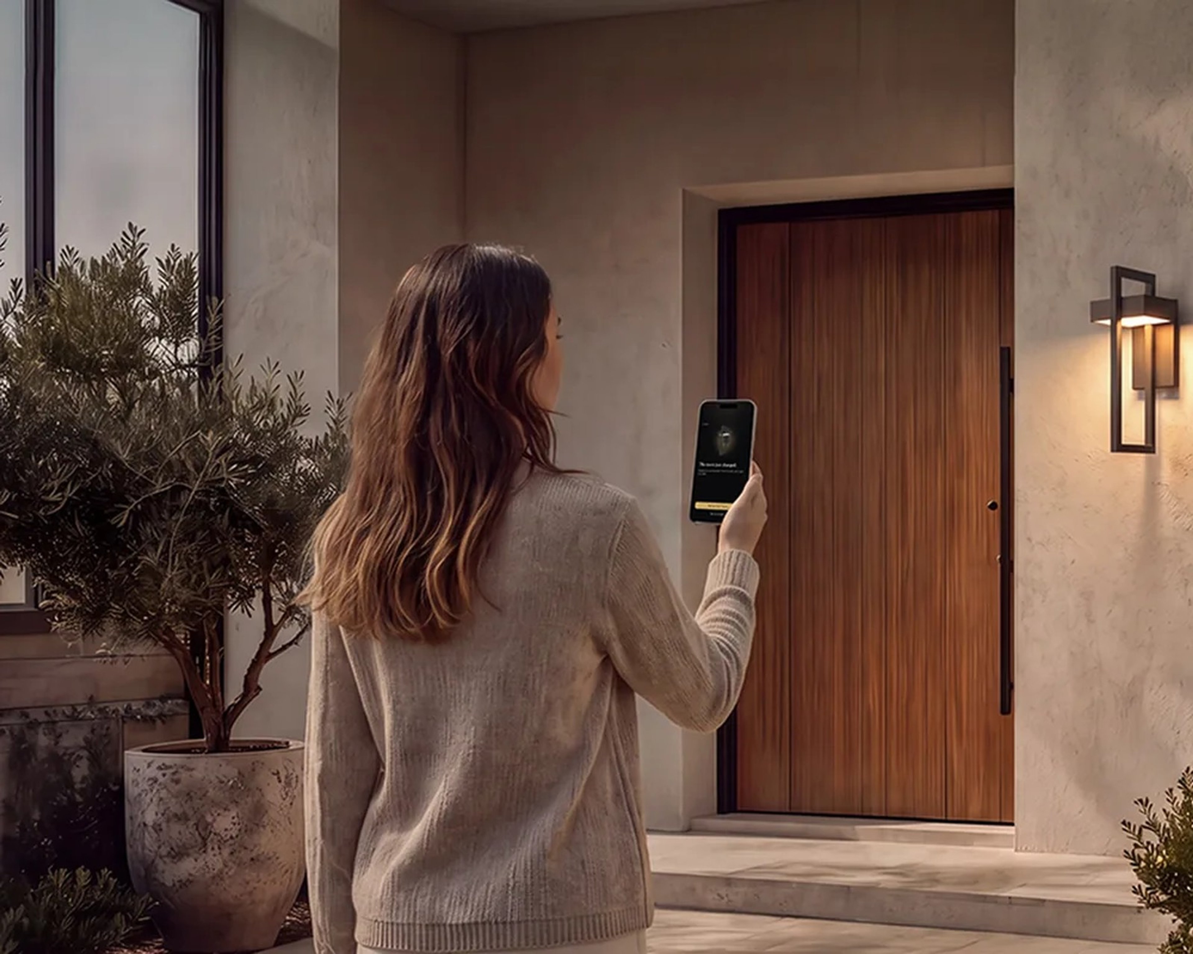 A woman opening the MOD LIGHTING app on her phone beside a lit outdoor wall sconce