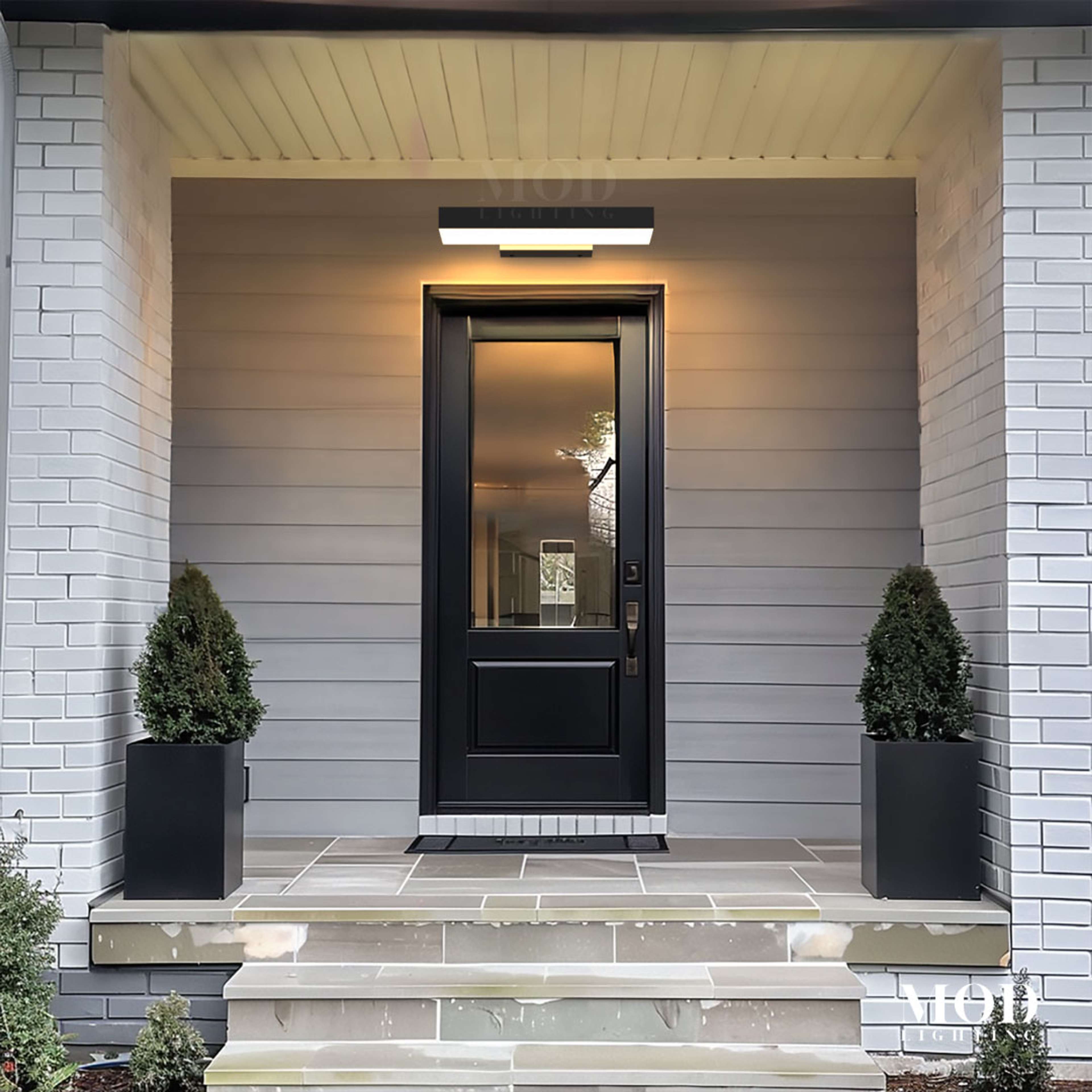 Brook black LED wall light, wide horizontal bar glowing above a glazed black front door on a covered porch