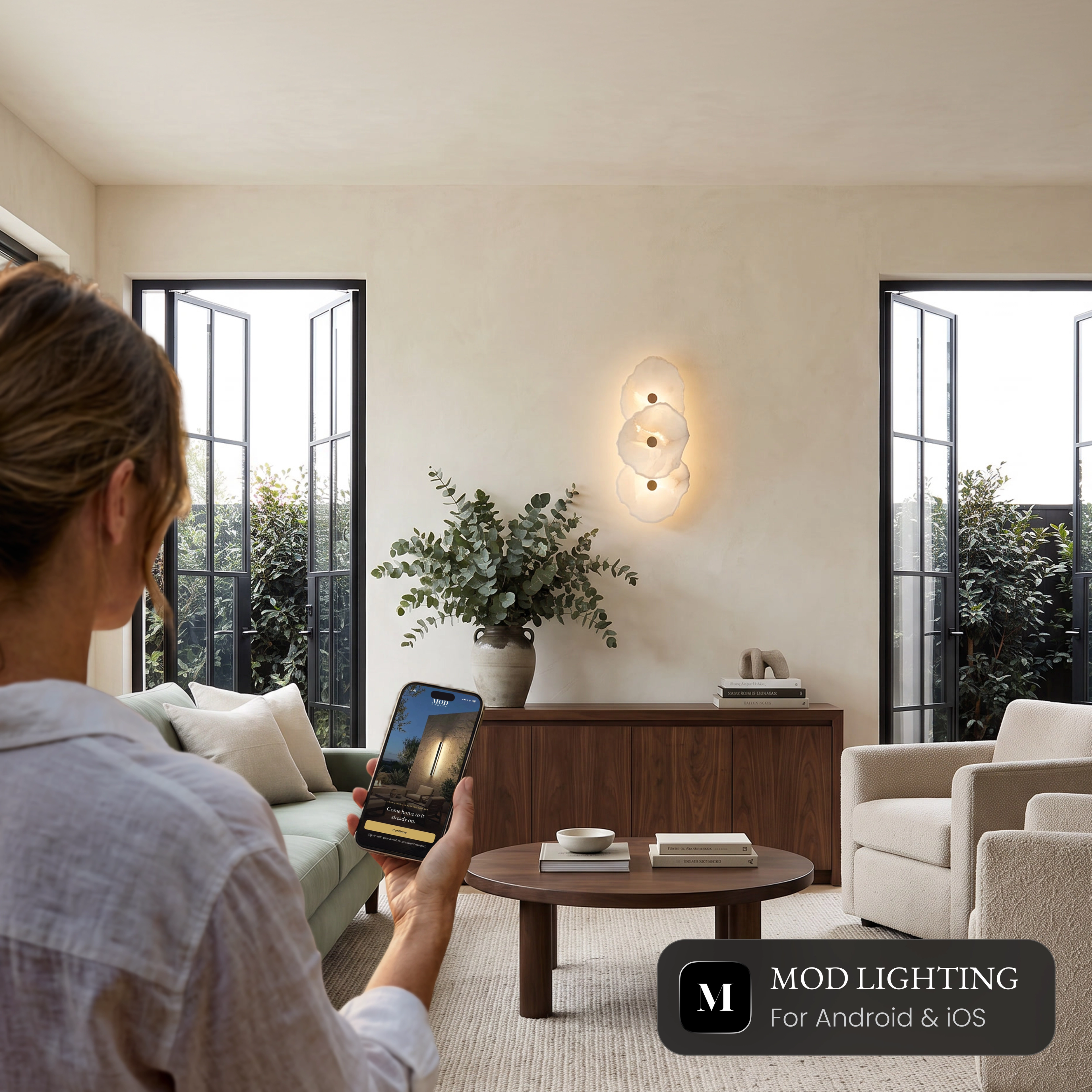 Alba Sconce Smart alabaster wall sconce in a living room, controlled from the MOD LIGHTING app on a phone