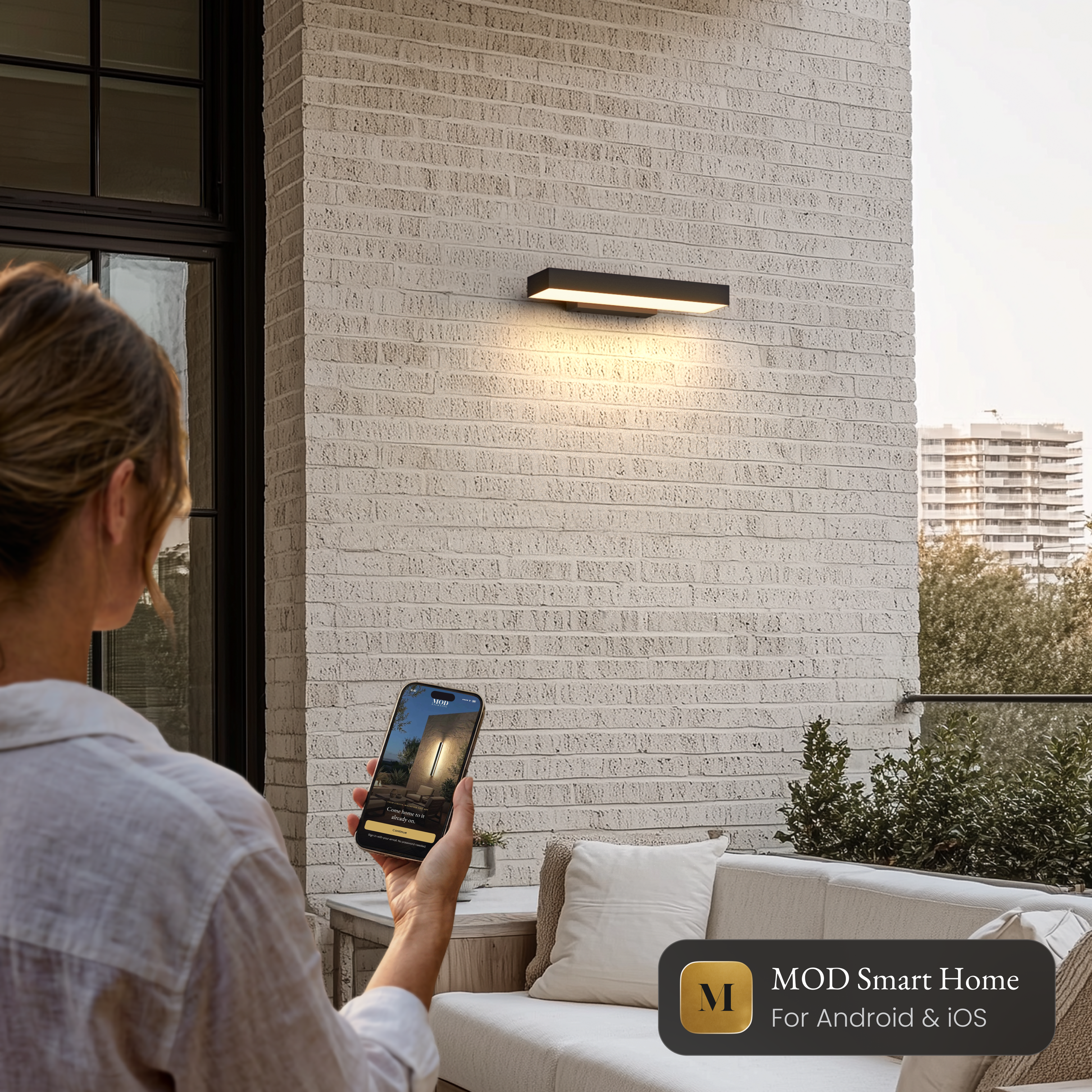 Brook Smart black horizontal outdoor sconce on a brick wall, controlled from the MOD Smart Home app on a phone