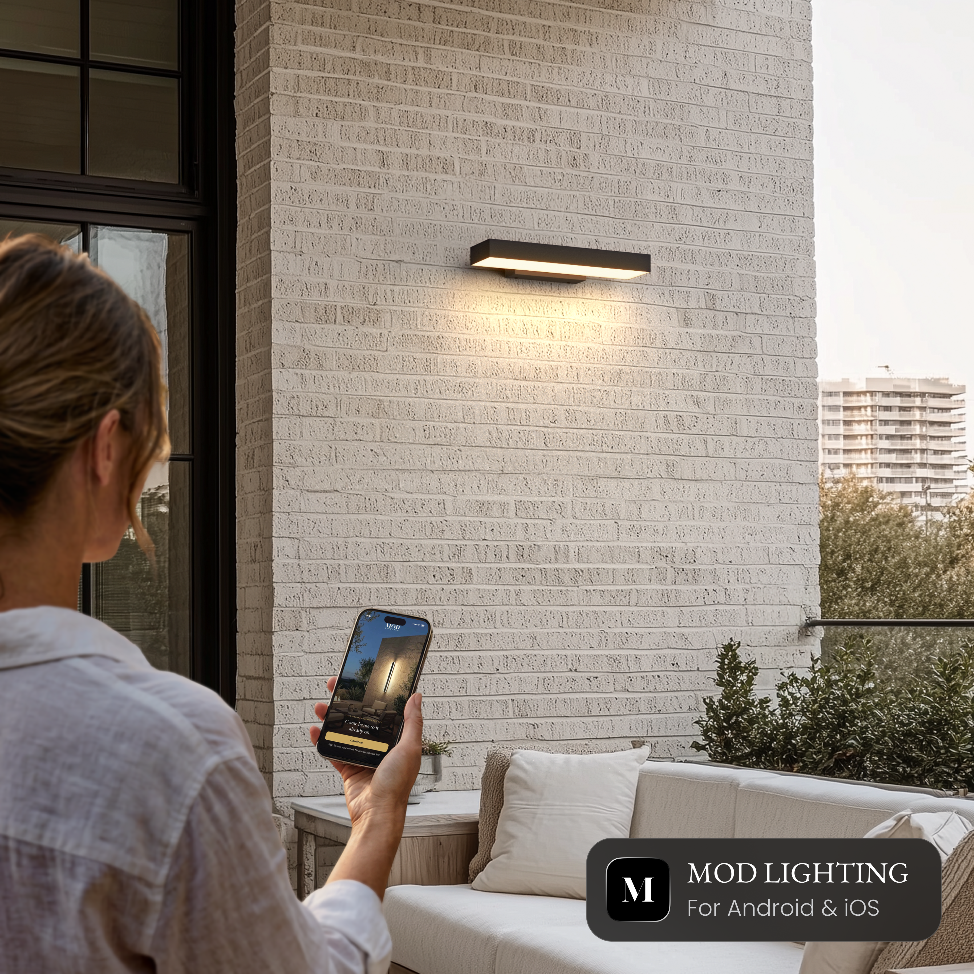 Brook Smart black horizontal outdoor sconce on a brick wall, controlled from the MOD LIGHTING app on a phone