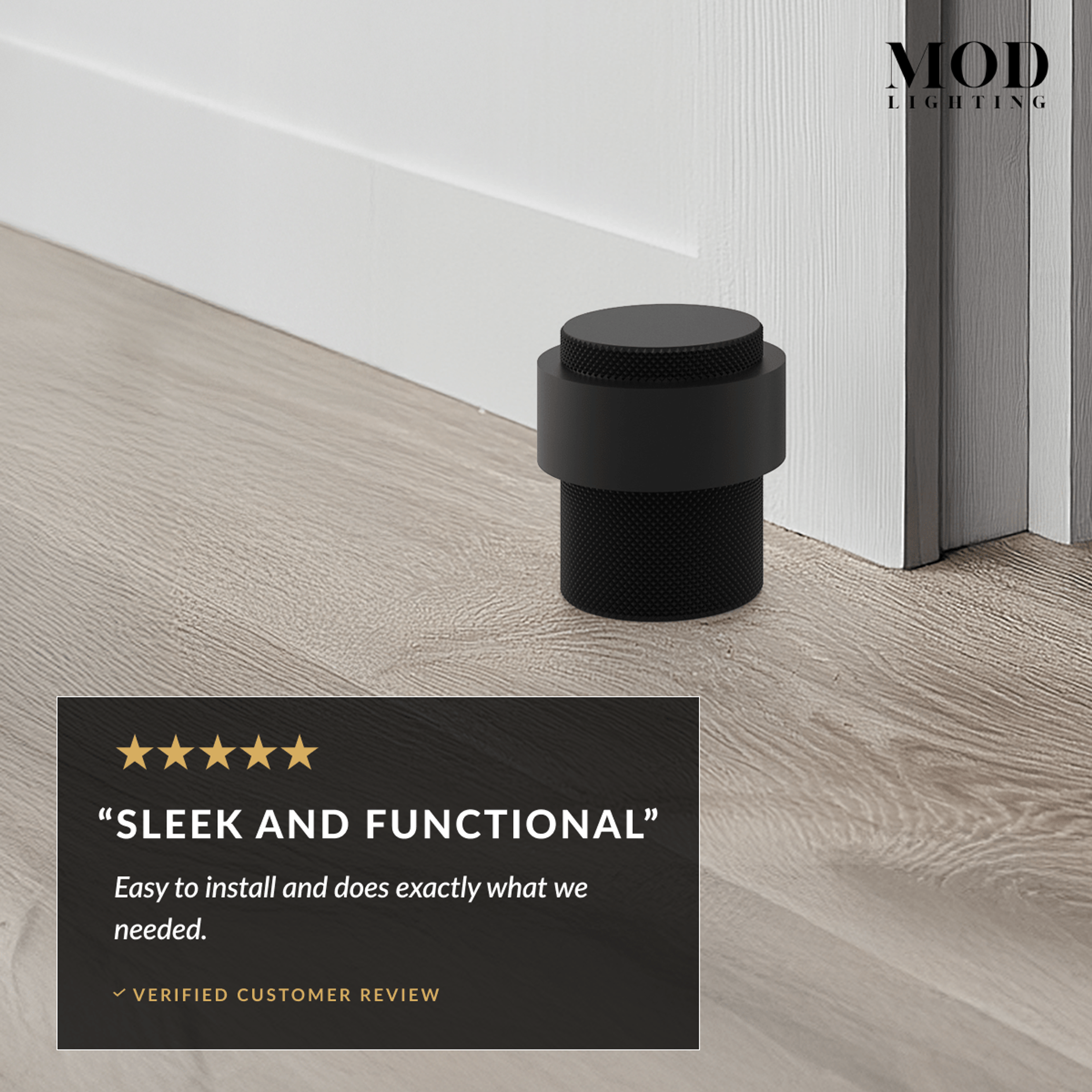 Enso matte black cylindrical door stop on a wood floor at the base of a door