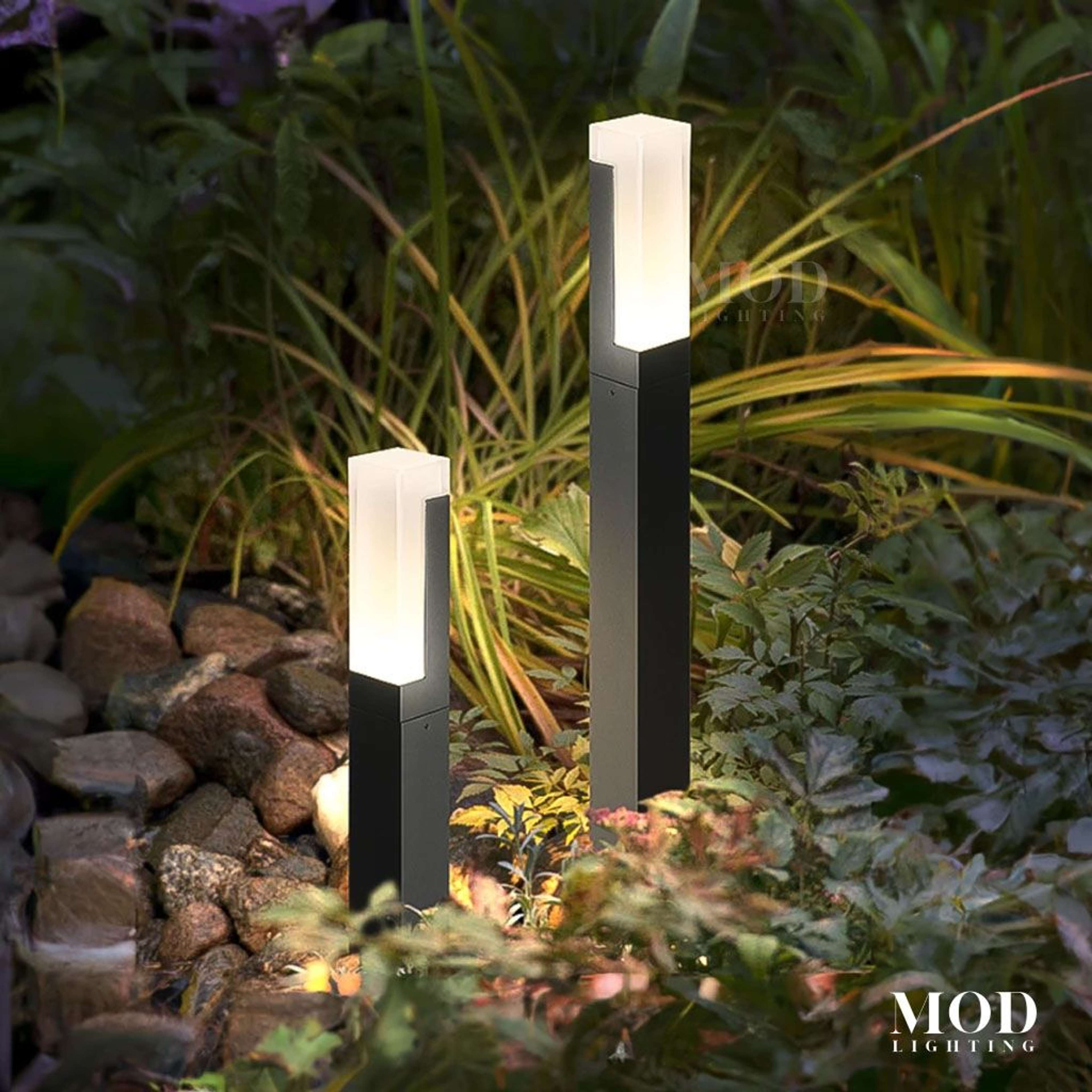 Meadow two black outdoor bollard path lights with frosted glowing tops among garden plants