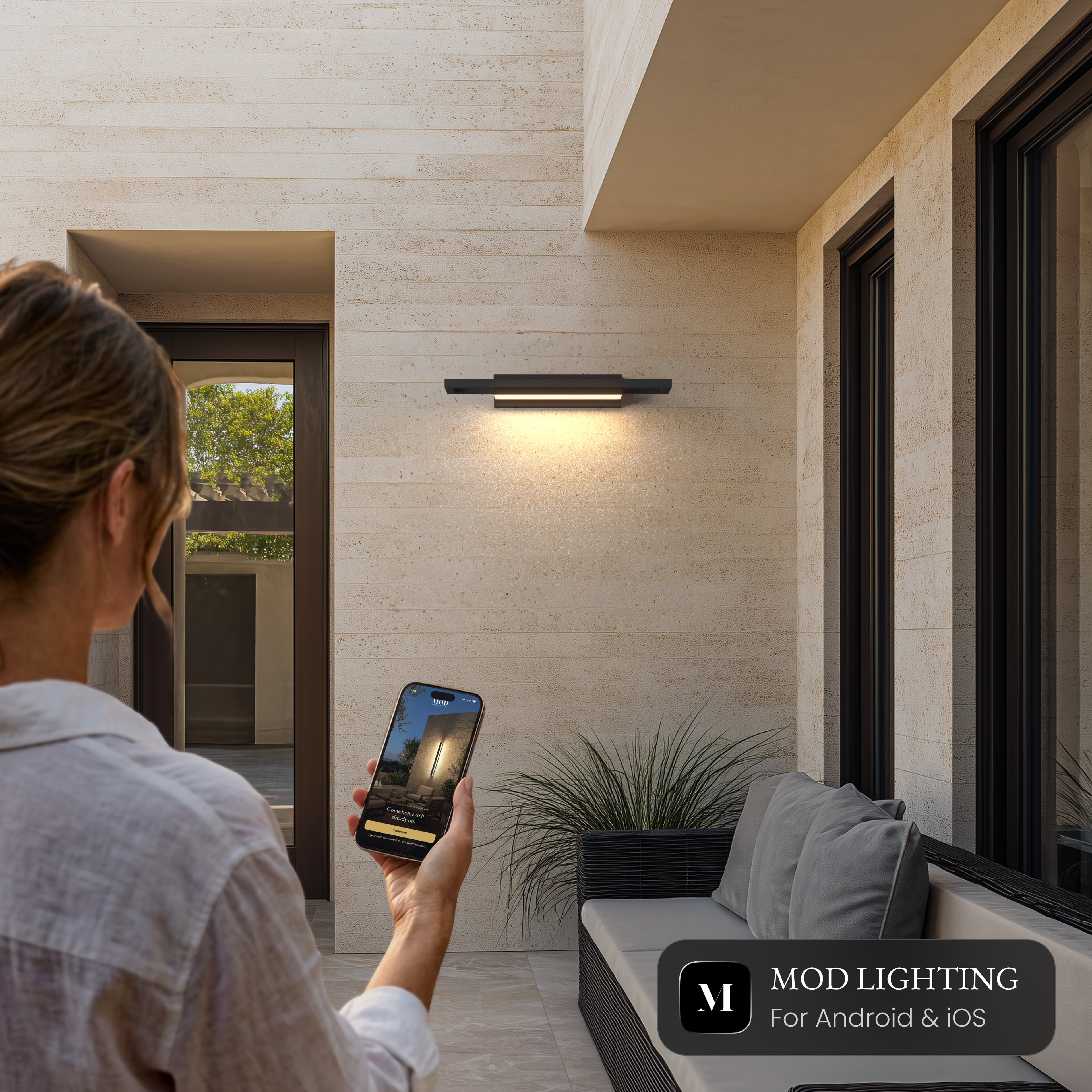 Brooklyn Smart black stainless outdoor sconce on a stone wall, controlled from the MOD LIGHTING app on a phone