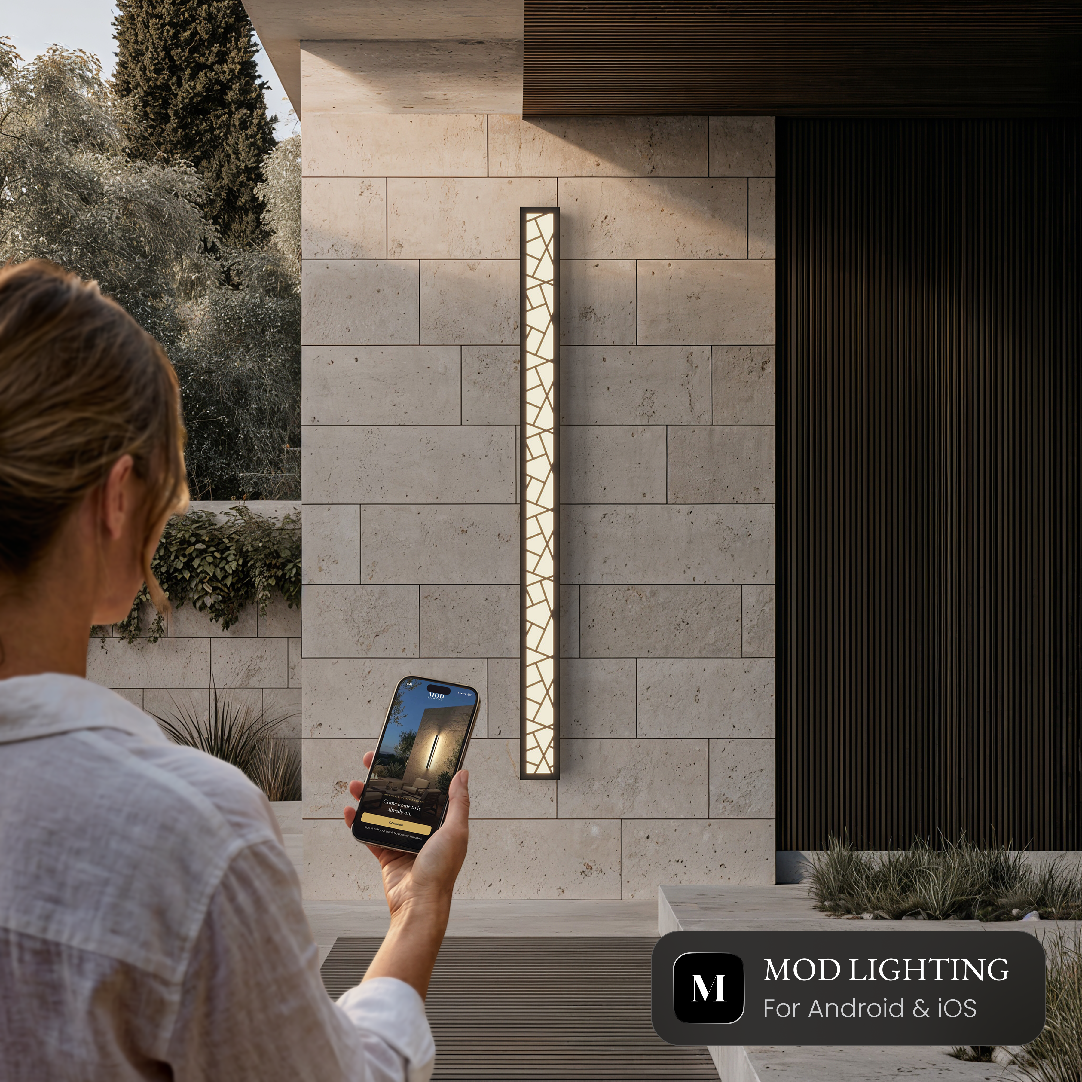 Harper Smart black LED bar wall light on a stone wall, controlled from the MOD LIGHTING app on a phone