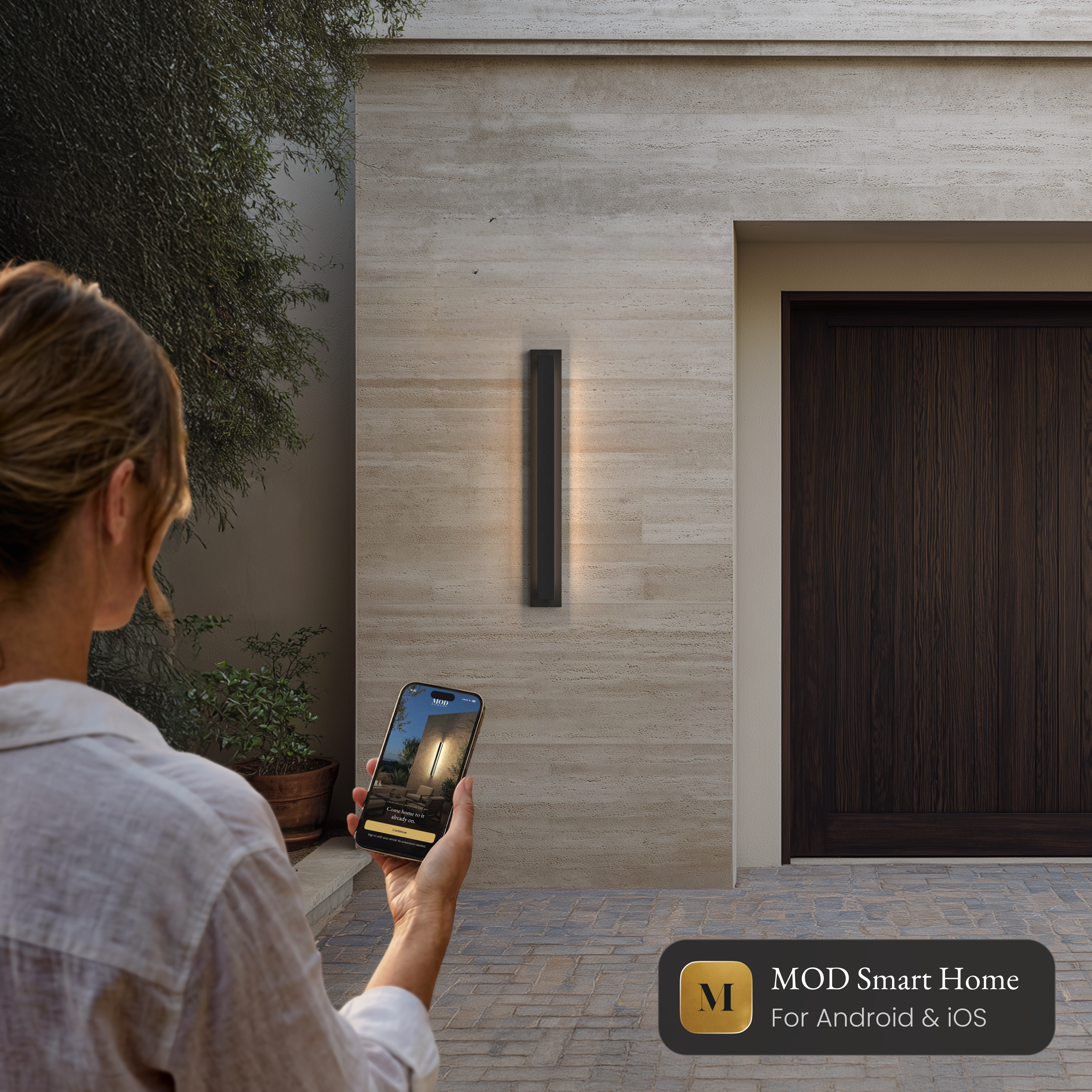 Vetra Smart black vertical LED sconce on a stone wall, controlled from the MOD Smart Home app on a phone